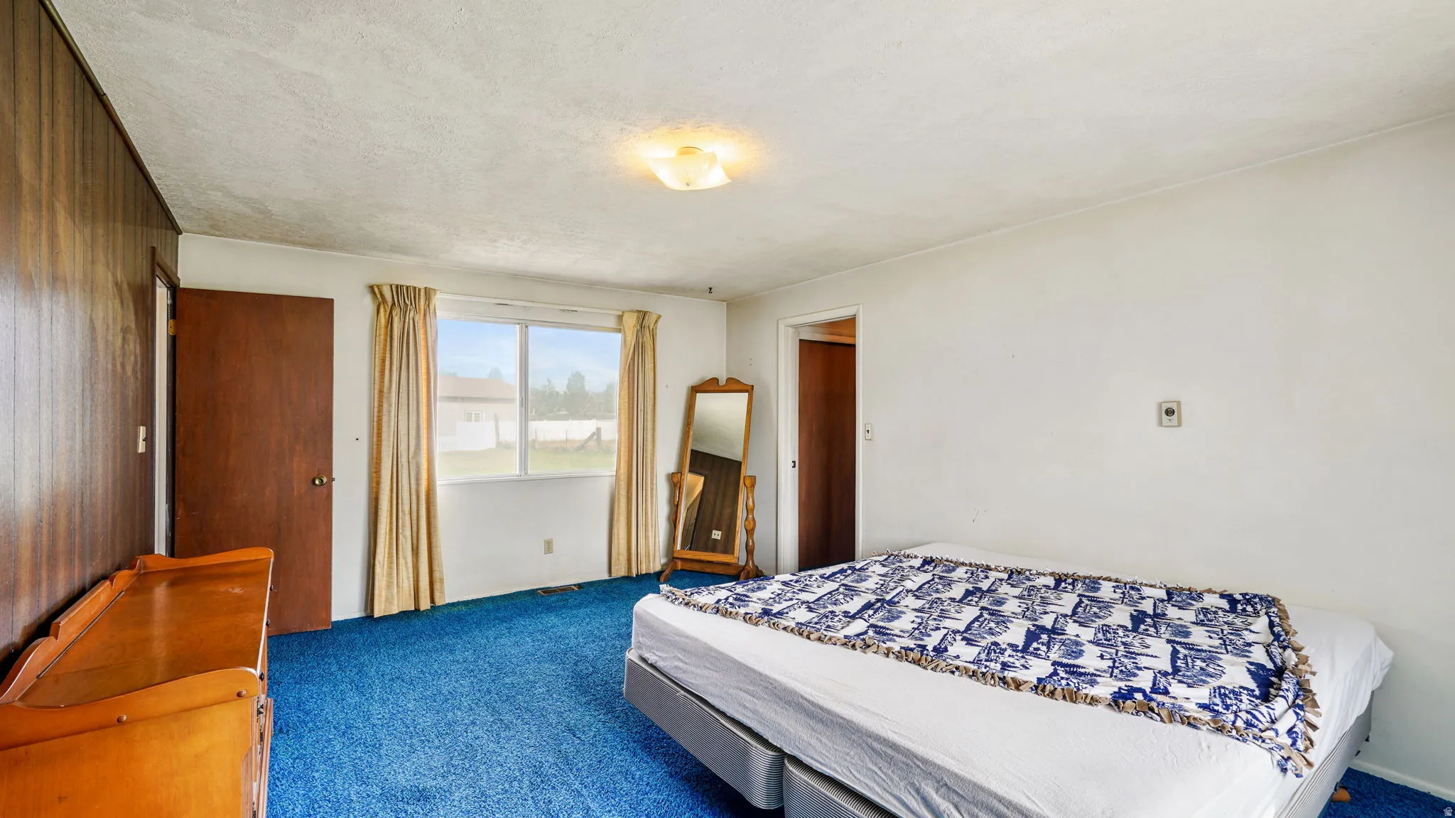 Bedroom featuring a large window, a ceiling-mounted light fixture, wood paneling, and blue carpeting
