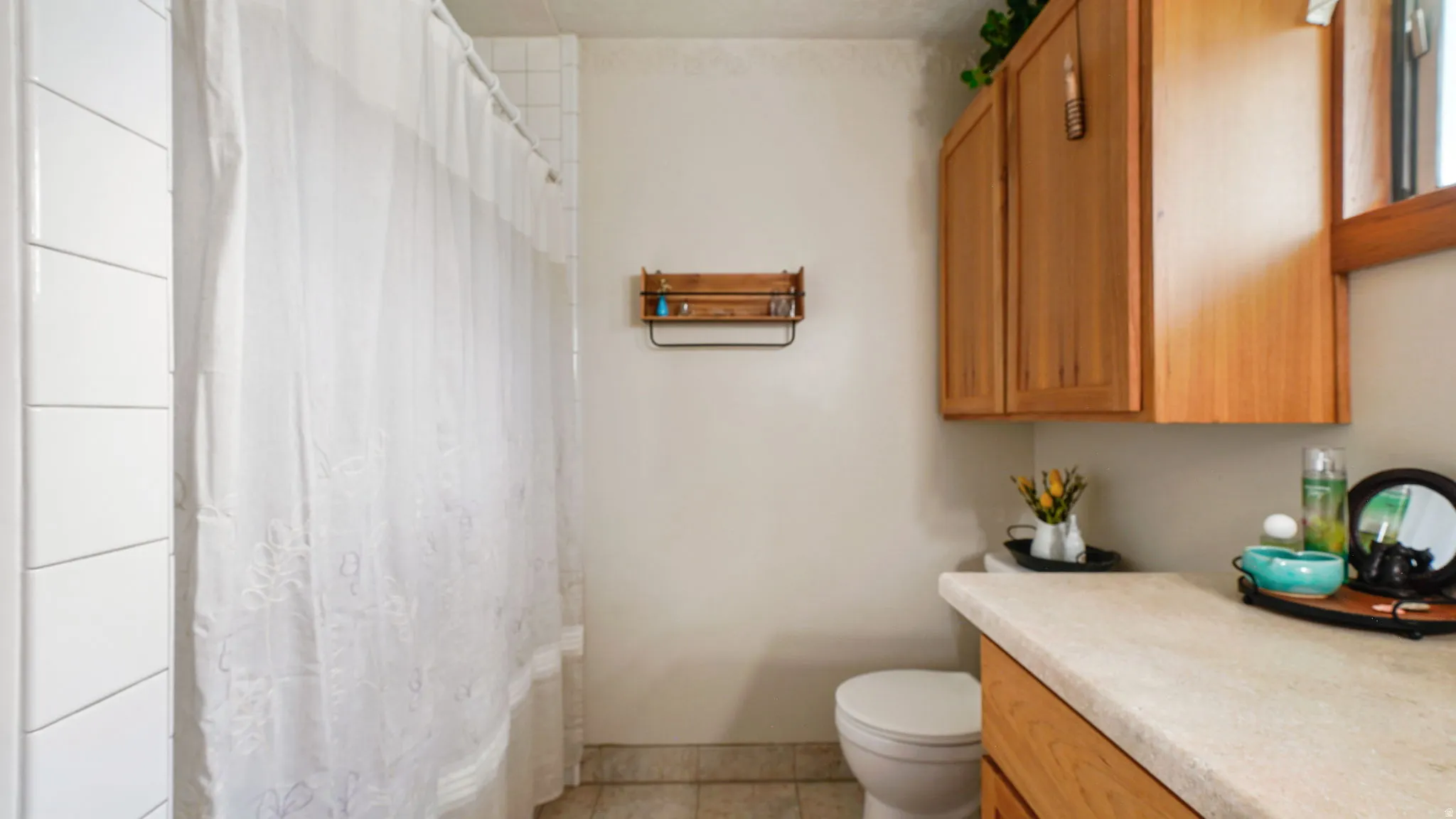 Bathroom featuring a tiled shower surround, light-toned countertop, wood-finish cabinetry, and a window for natural light