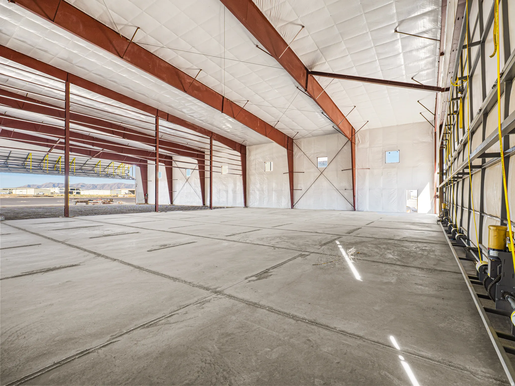 Spacious industrial interior featuring a concrete floor, exposed structural beams, insulated ceiling panels, and several window openings