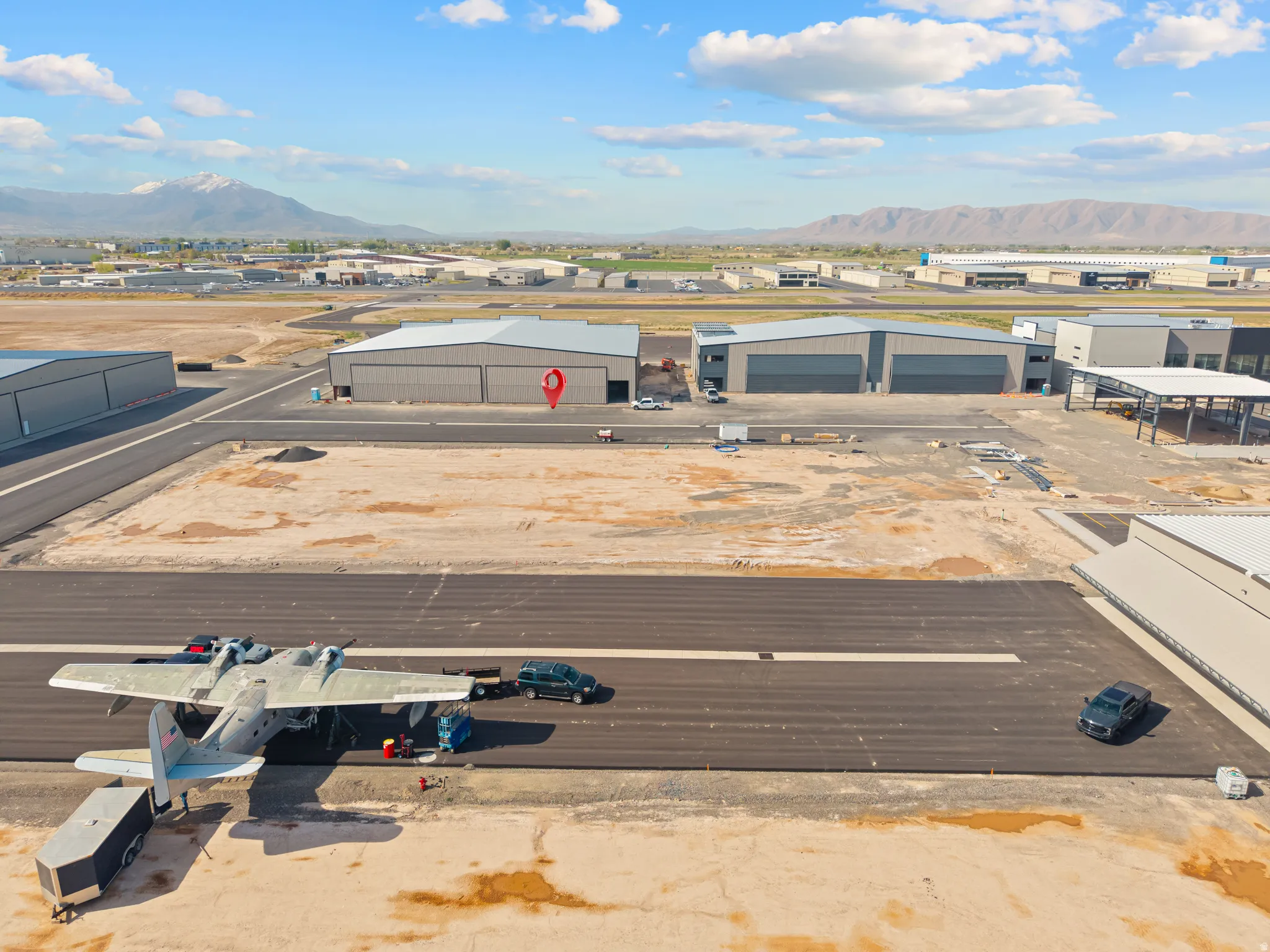 Expansive airfield featuring a newly paved runway, multiple large hangars, and undeveloped land