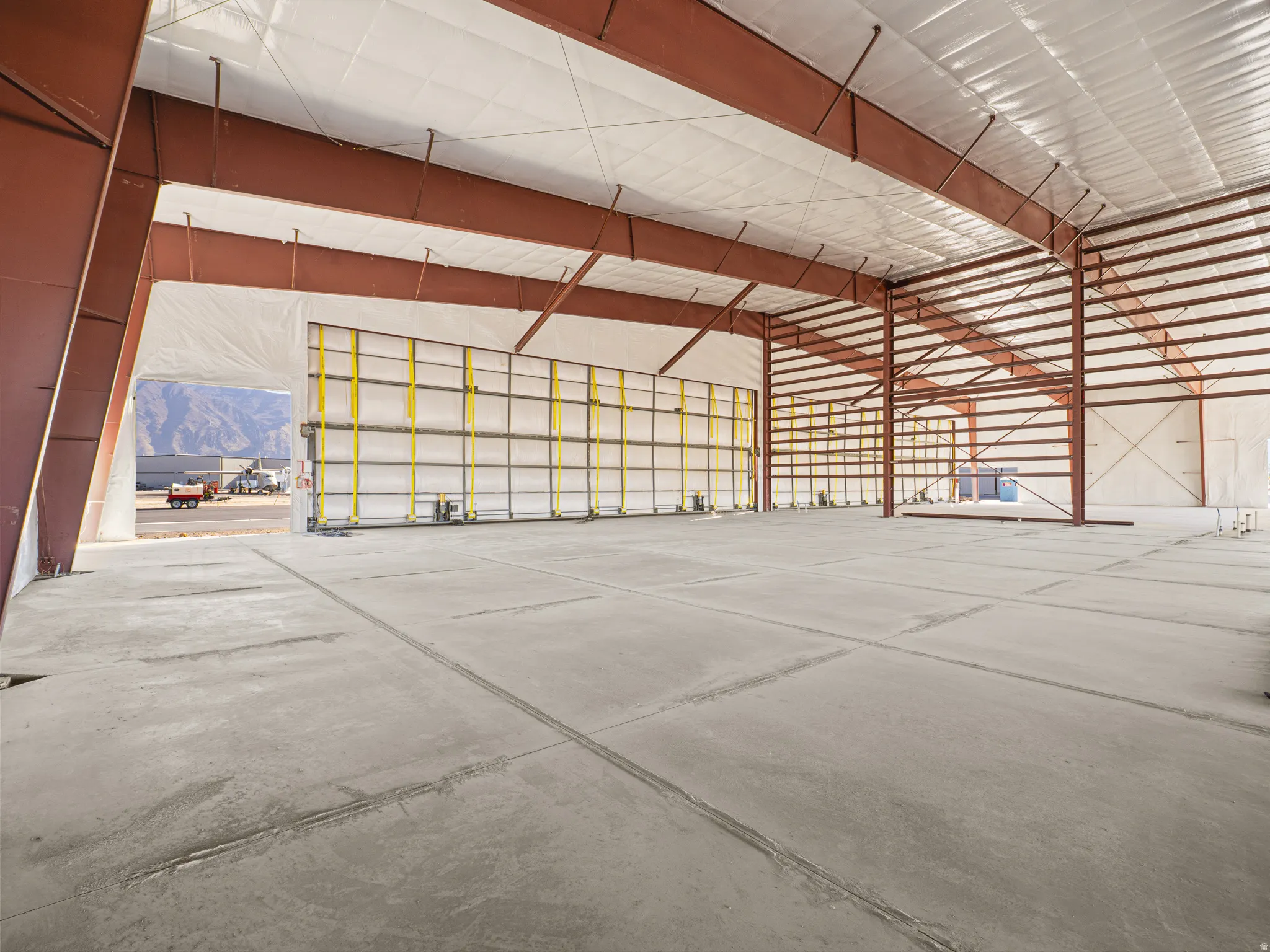 Spacious industrial interior featuring an expansive concrete floor, visible structural steel beams, high ceilings with insulated roofing, and a large roll-up door
