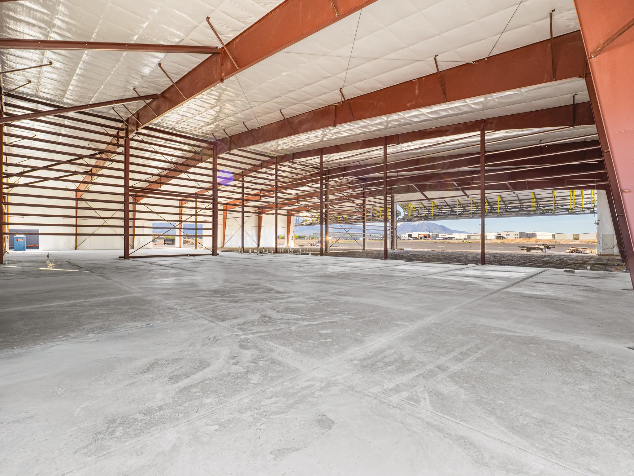 Spacious commercial shell with exposed steel beam construction, insulated ceiling, concrete flooring, and ample natural light