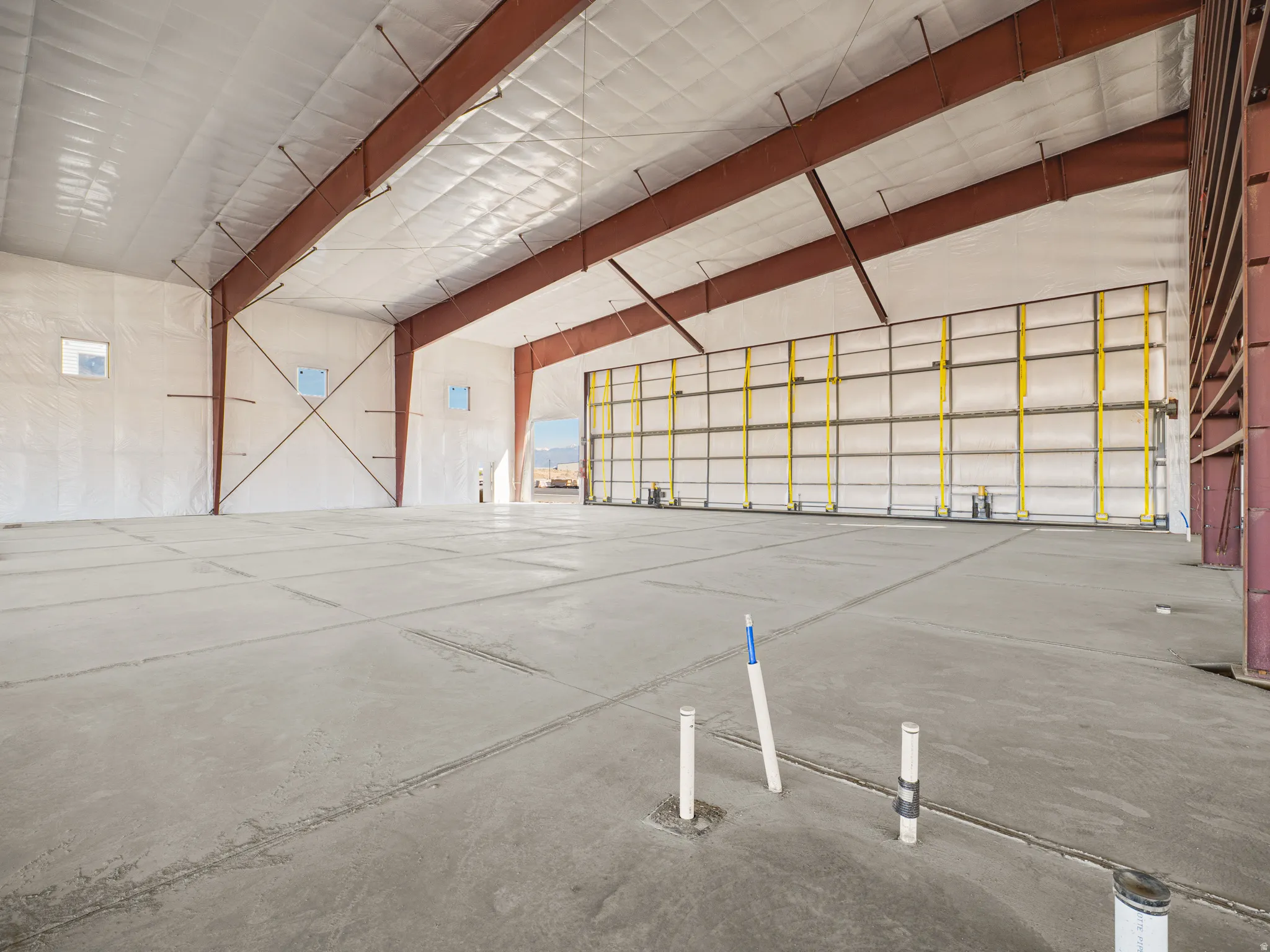 Expansive industrial space featuring a concrete floor, exposed structural beams, and insulated walls