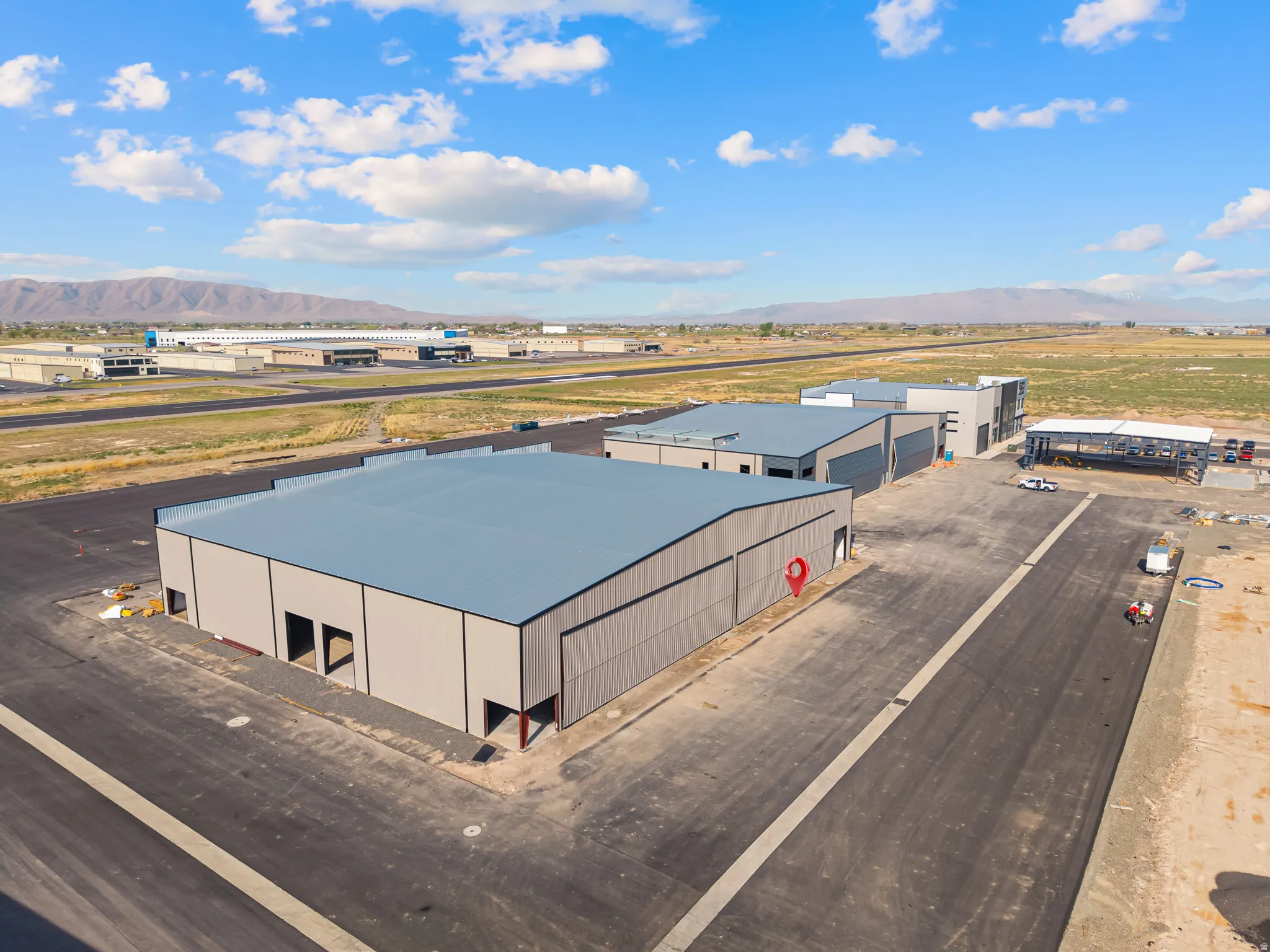 Expansive commercial property featuring multiple industrial buildings with metal siding and roofs, large garage door openings, newly paved lot, and mountain backdrop