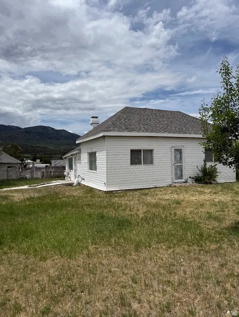 White siding exterior with a brown shingle roof, featuring multiple windows and a mountain backdrop