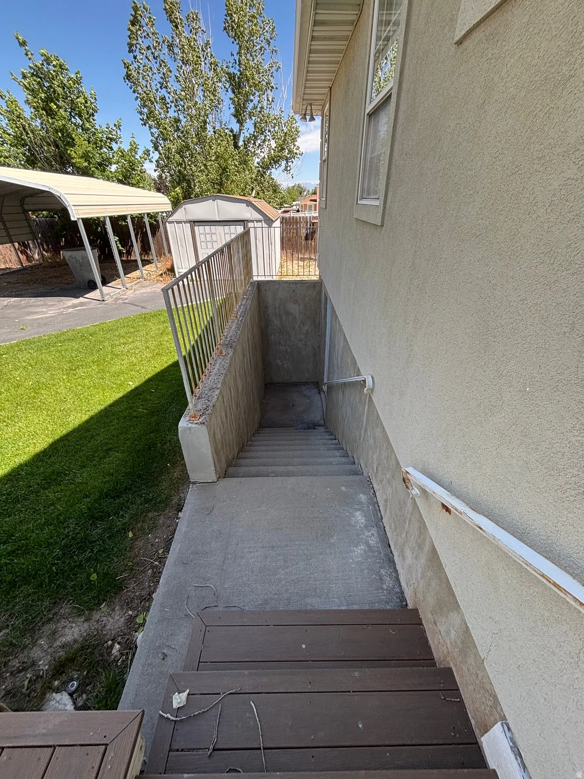 Exterior access to lower level featuring concrete steps, metal railing, and a stucco-finish wall