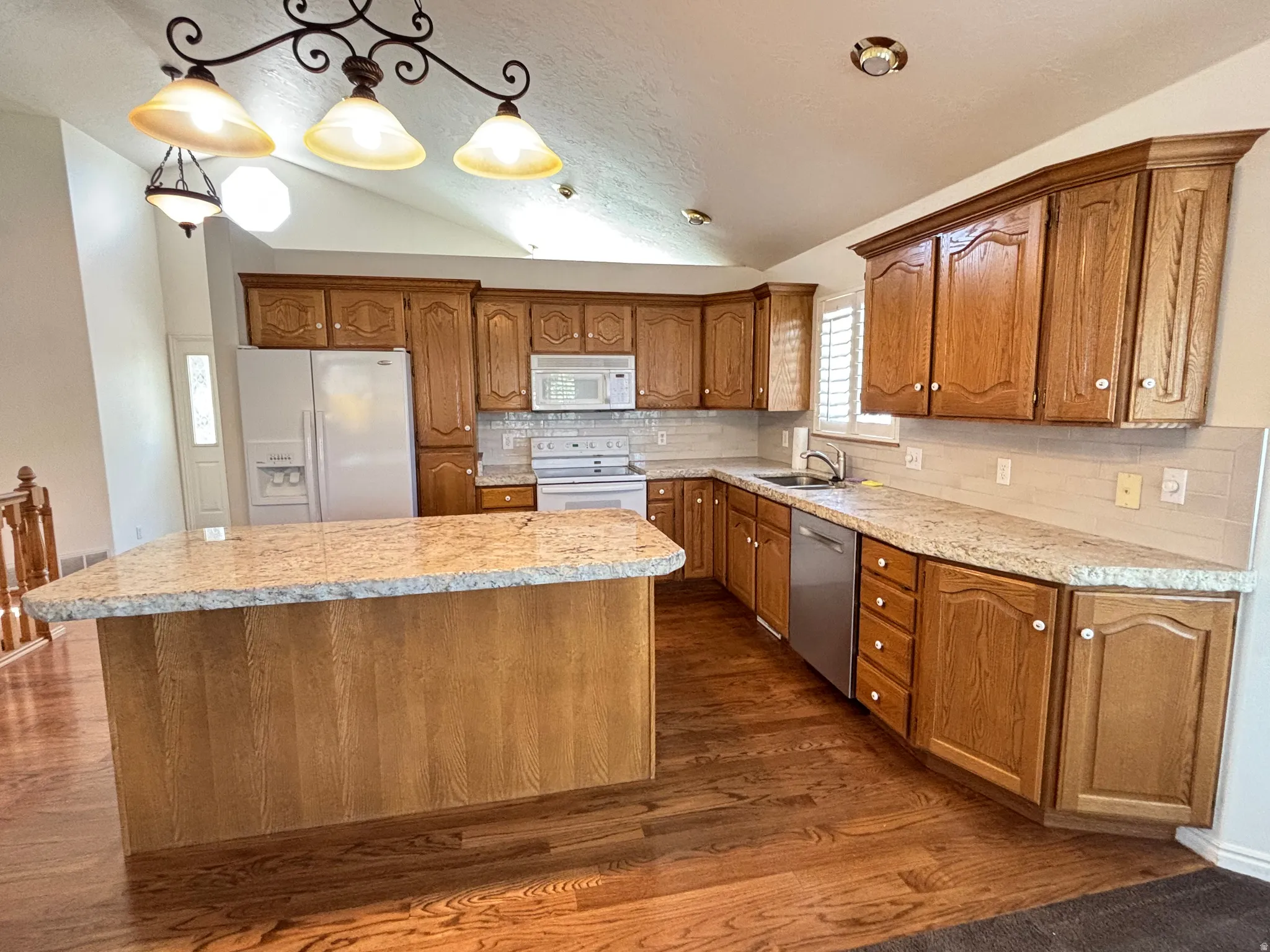 Kitchen featuring granite-look countertops, wood-finish cabinetry, tile backsplash, and stainless steel appliances
