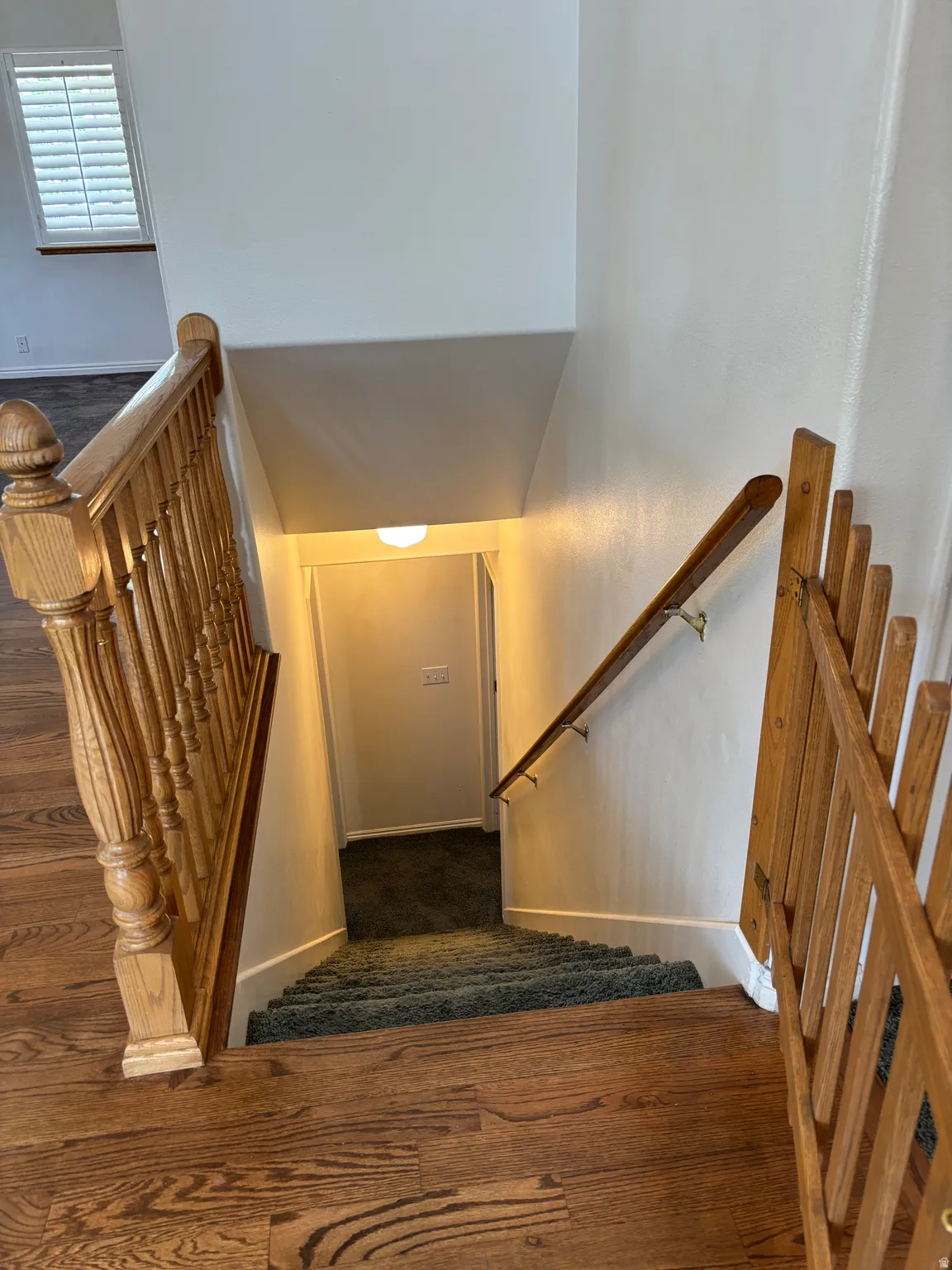 Wood-finish flooring leading to a carpeted staircase with a wooden handrail