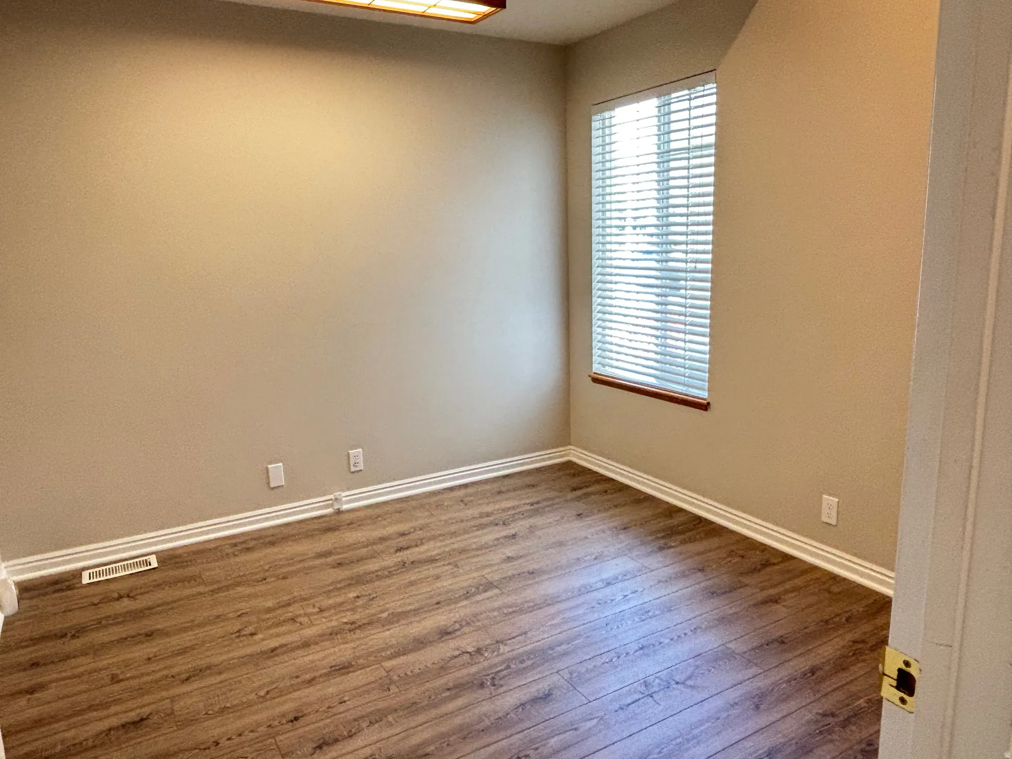 Room featuring wood-finish flooring, a window with horizontal blinds, and a ceiling-mounted light fixture