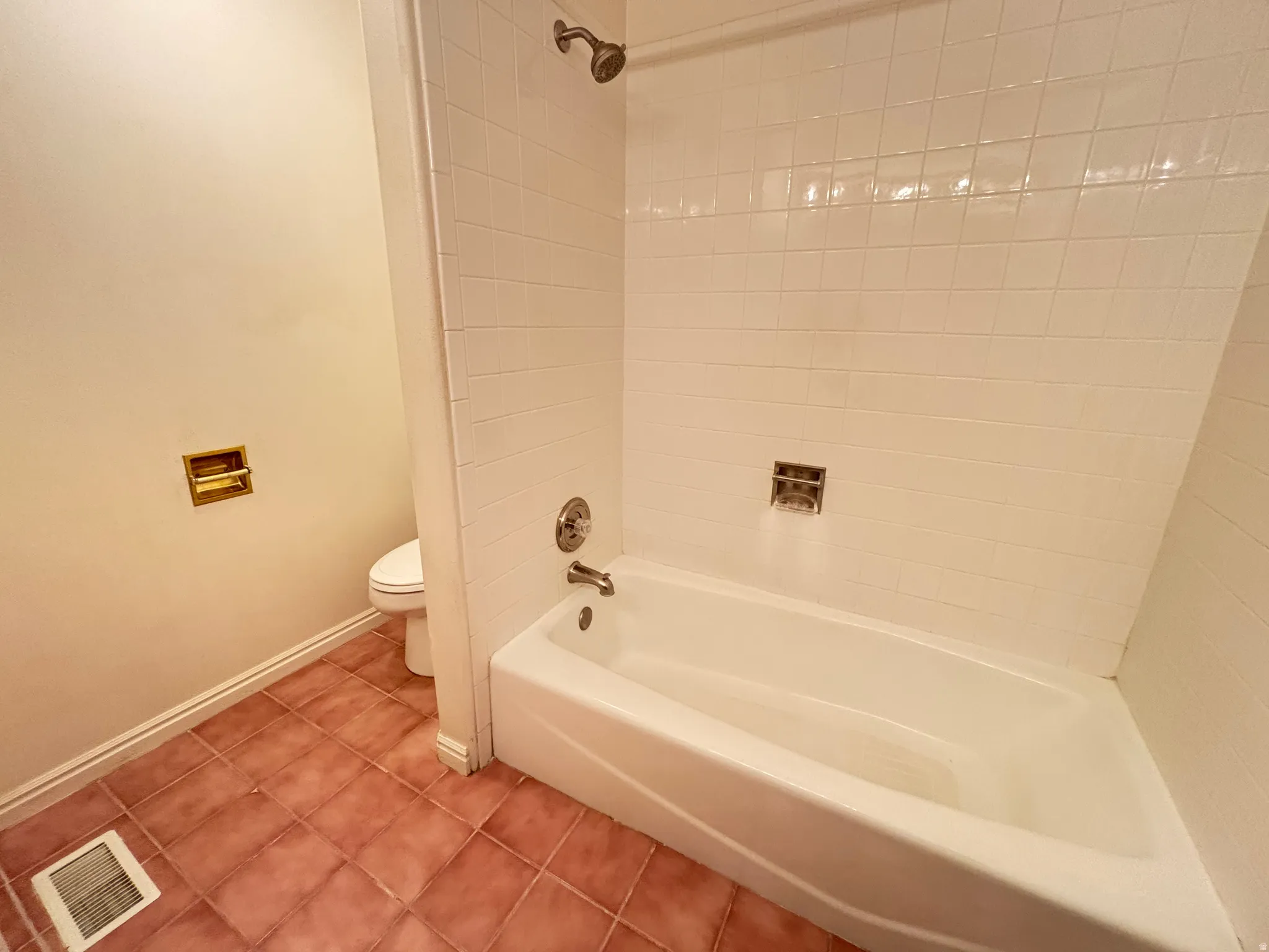 Bathroom featuring a white tub, shower with ceramic tile surround, and terra cotta floor tiles