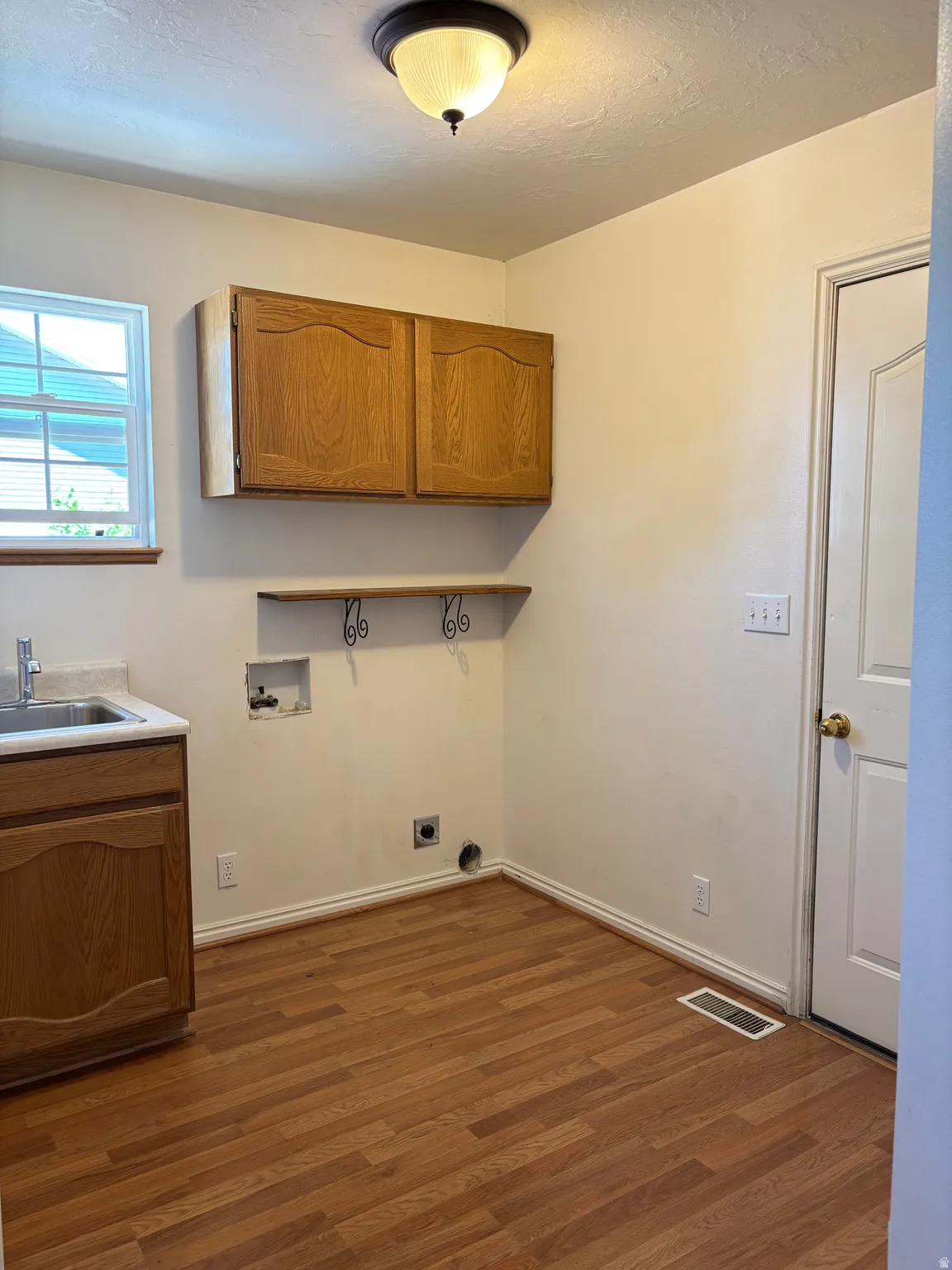 Laundry area featuring wood-finish flooring, a utility sink with base cabinetry, wall-mounted upper cabinetry, and a ceiling-mounted light fixture
