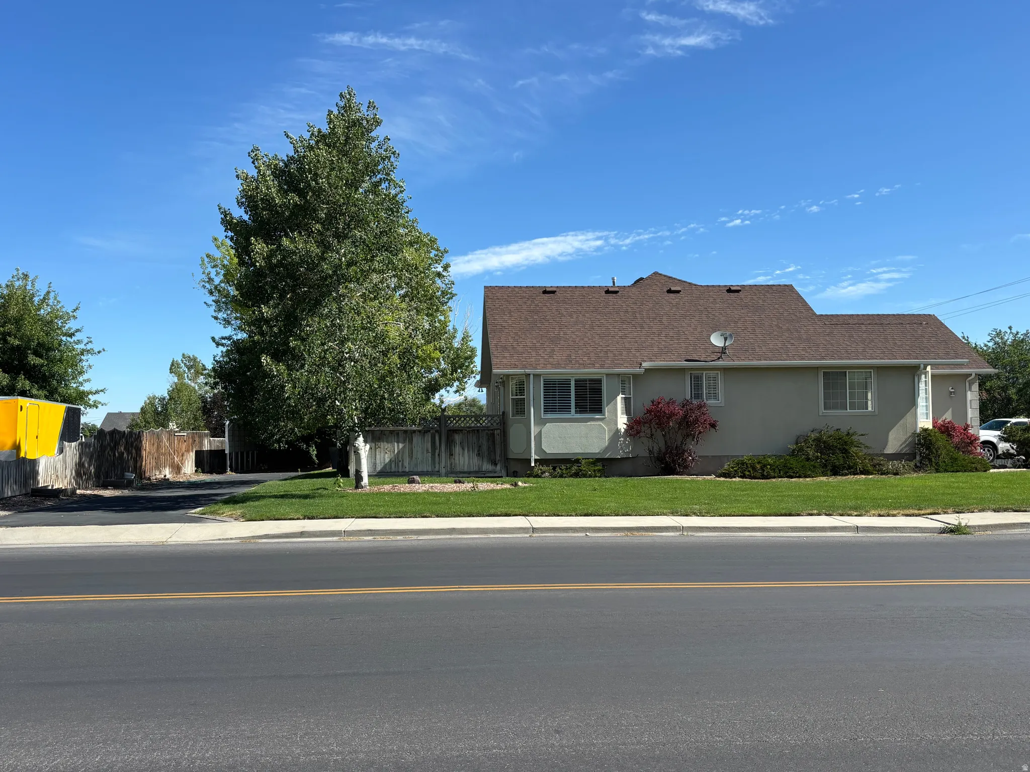 Stucco-sided residence featuring a brown shingle roof and a green lawn