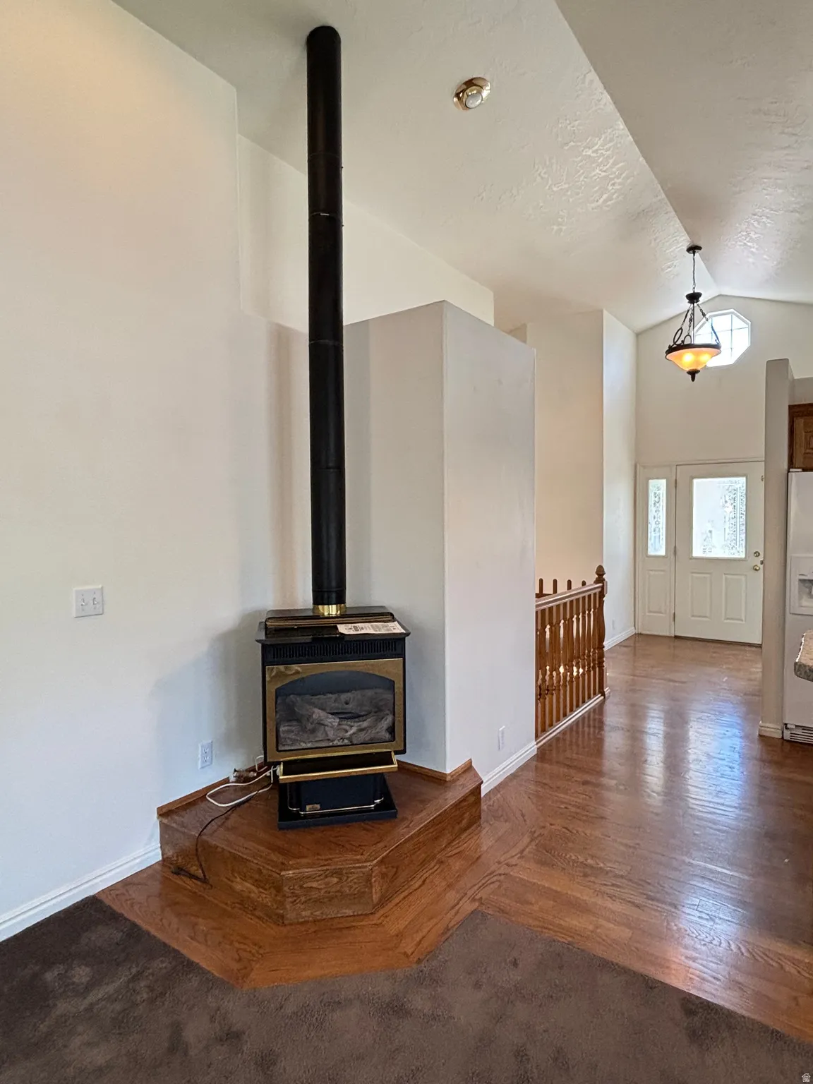 Corner fireplace with wood-finish hearth, dark wood-finish flooring, white walls, and a wood banister