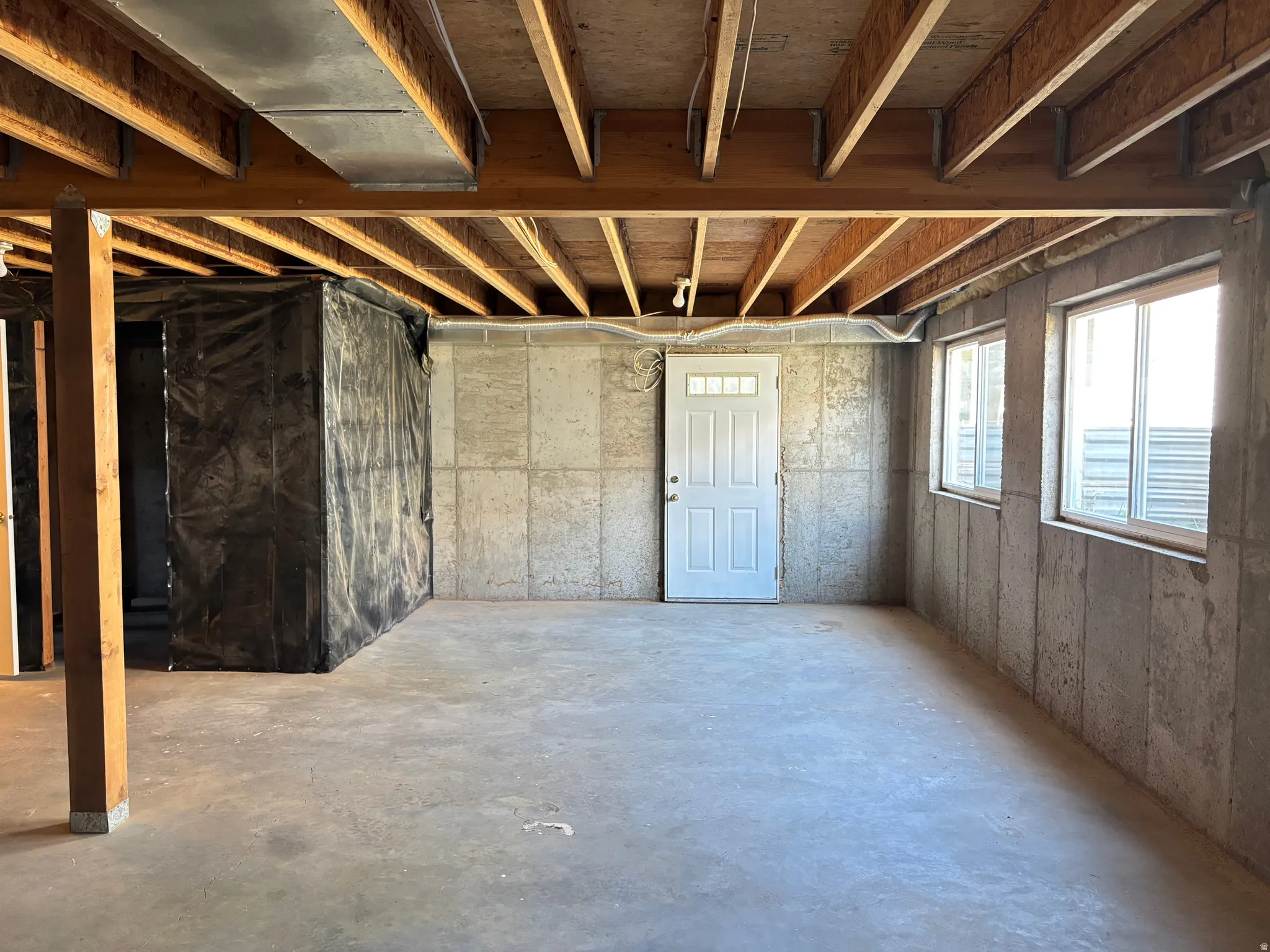Unfinished basement space featuring exposed wooden ceiling joists, concrete flooring, and concrete block walls