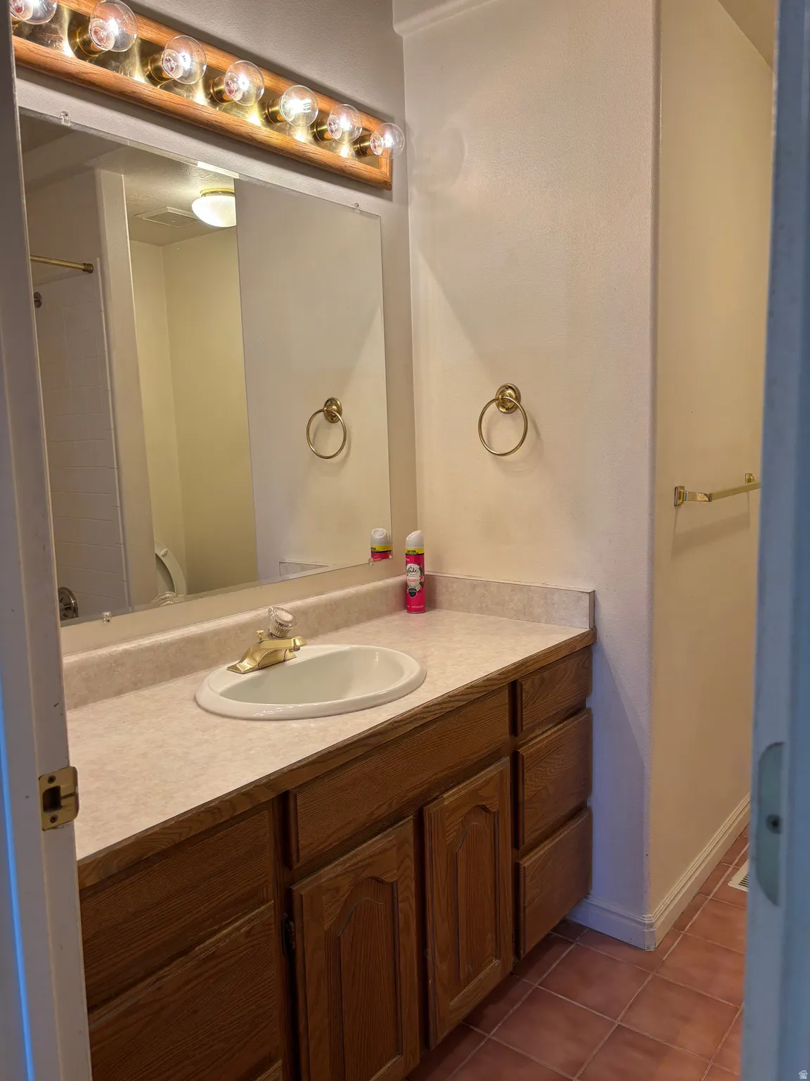 Bathroom vanity featuring a light-toned countertop with an integrated sink, wood-finish cabinetry, and a framed mirror
