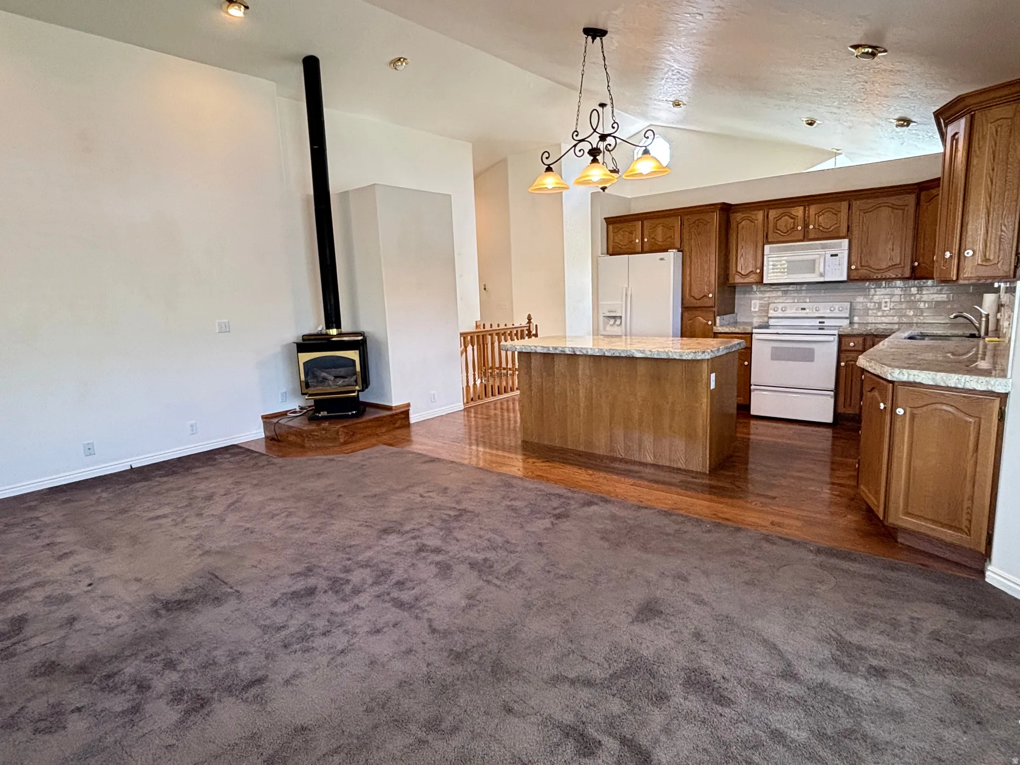 Open concept living area featuring a wood-burning stove on a raised hearth, vaulted ceiling, recessed lighting, and a chandelier