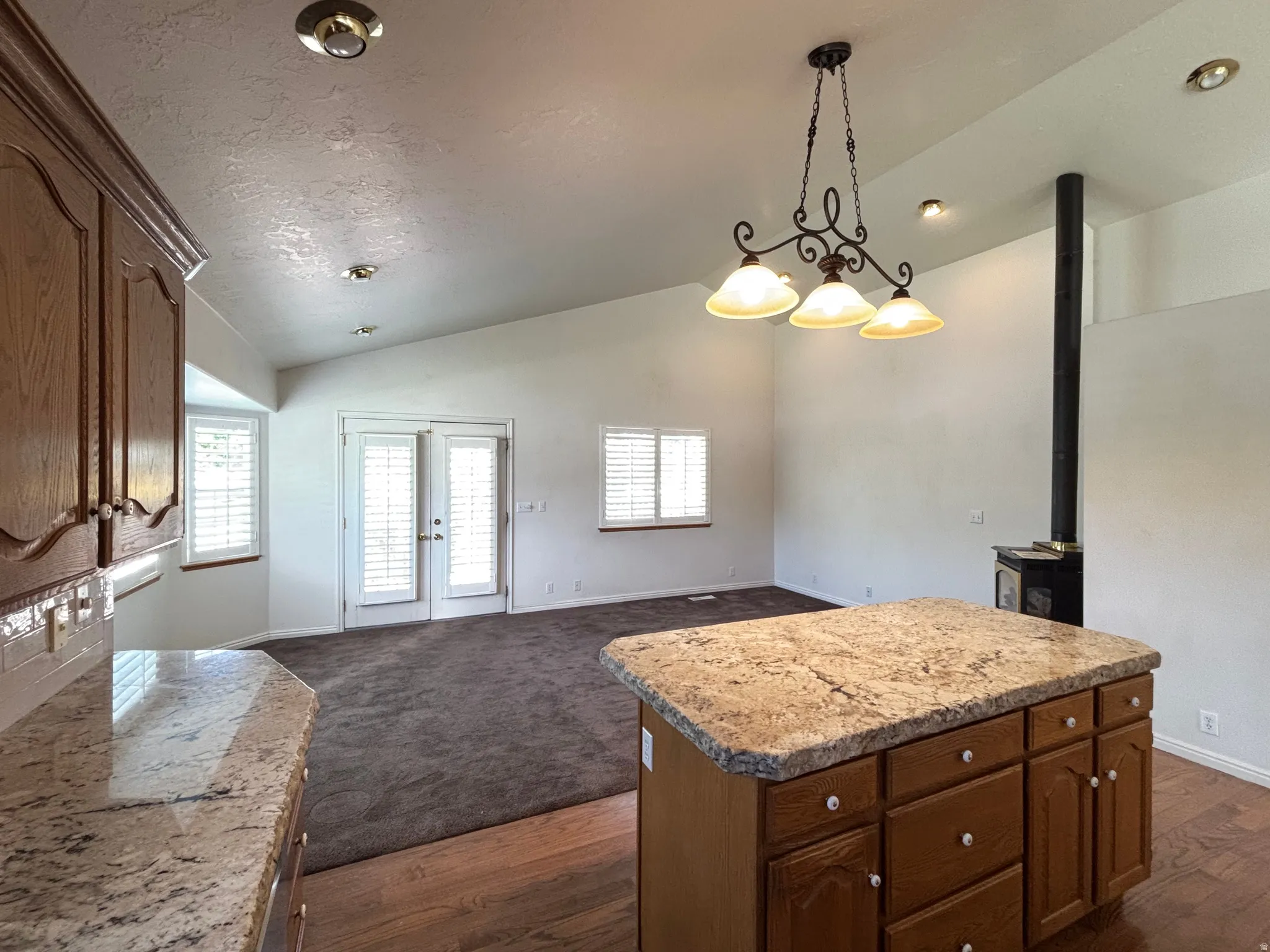 Kitchen island with granite countertop and wood cabinetry, open to a living area with vaulted ceilings, recessed lighting, and a wood-burning stove
