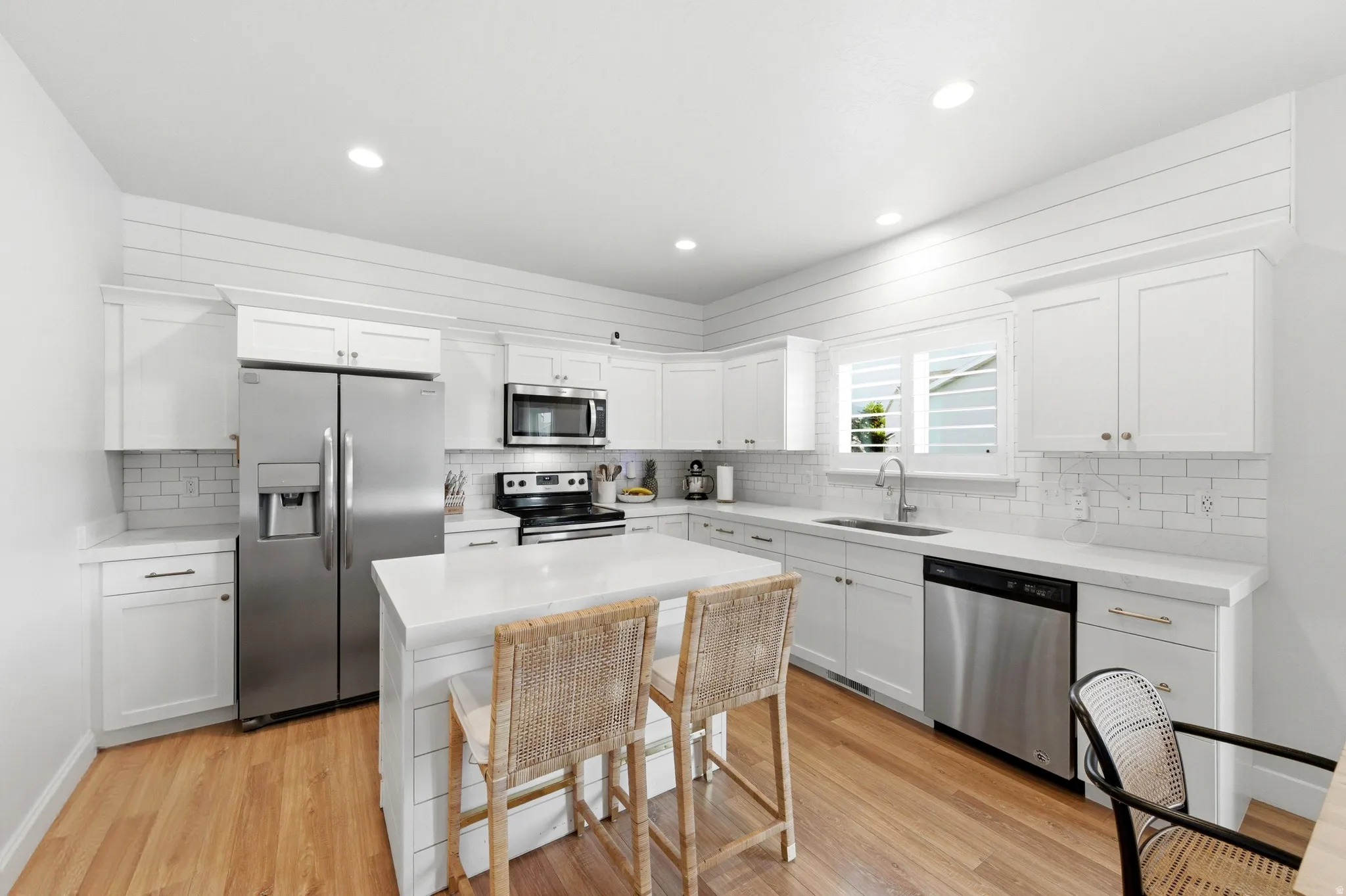 Modern kitchen featuring a central island, white cabinetry, stainless steel appliances, and wood-finish flooring