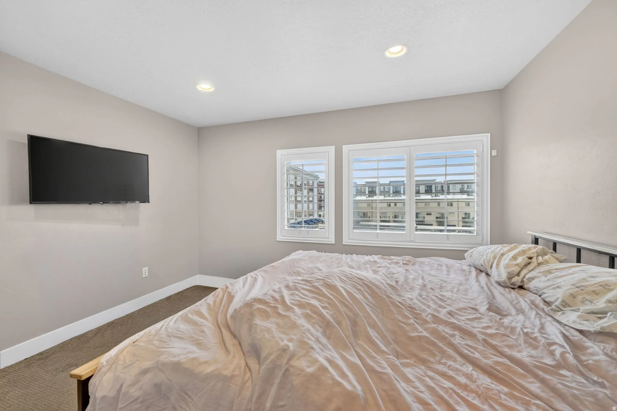 Neutral-toned room featuring two windows with white plantation shutters, recessed ceiling lighting, and light-toned wall paint