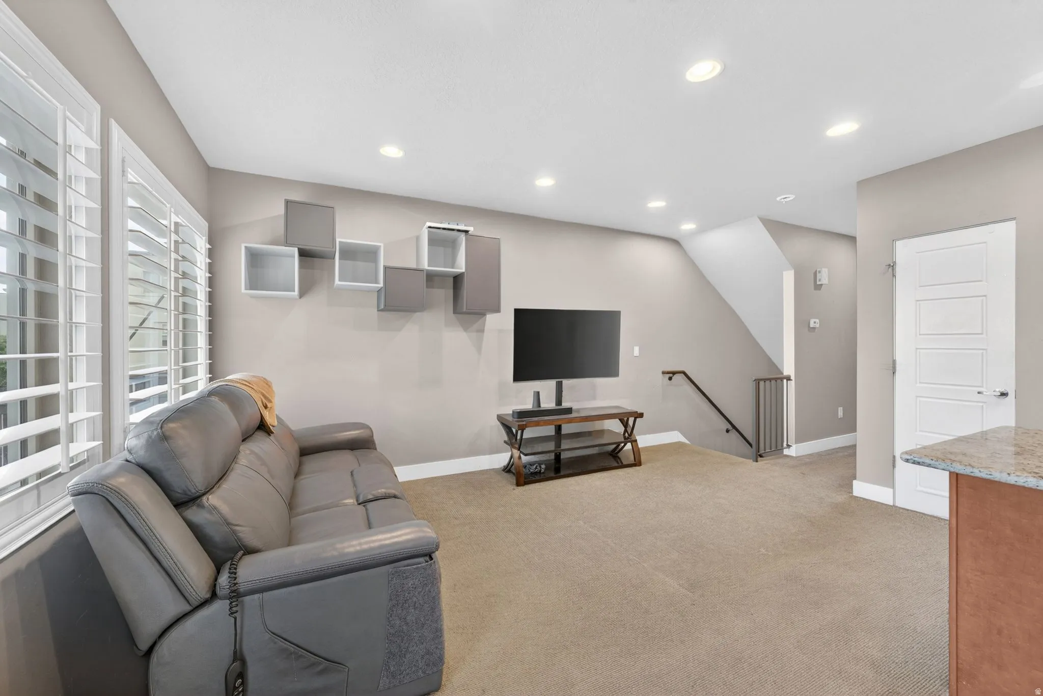 Living area featuring neutral-toned carpet flooring, recessed lighting, and a staircase with a metal railing