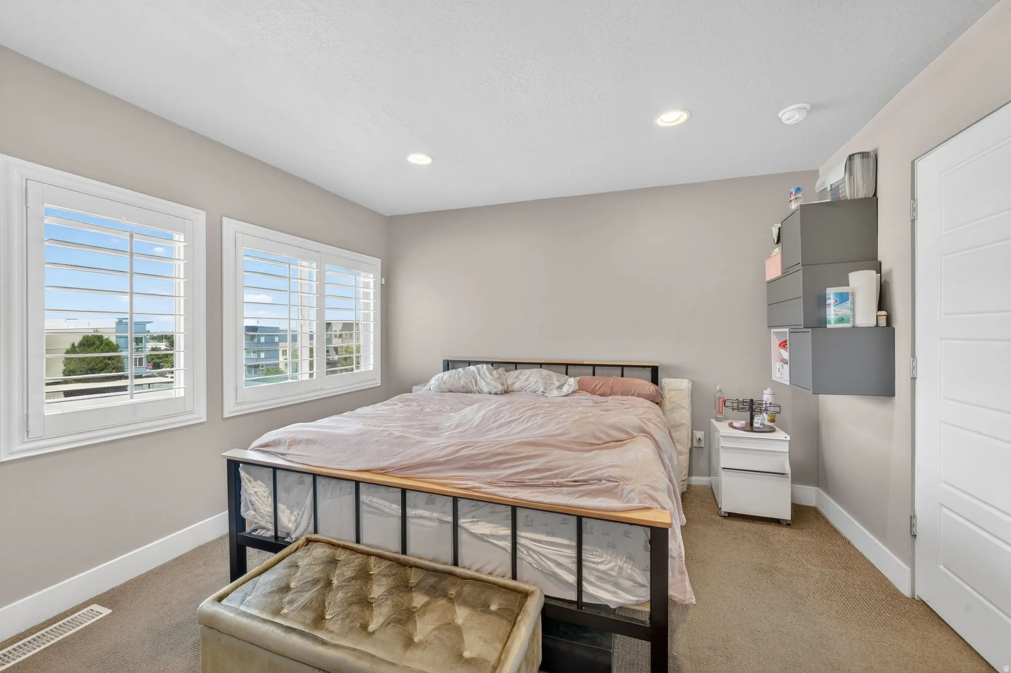Bright bedroom featuring two windows with white plantation shutters, neutral wall paint, recessed lighting, and carpet flooring