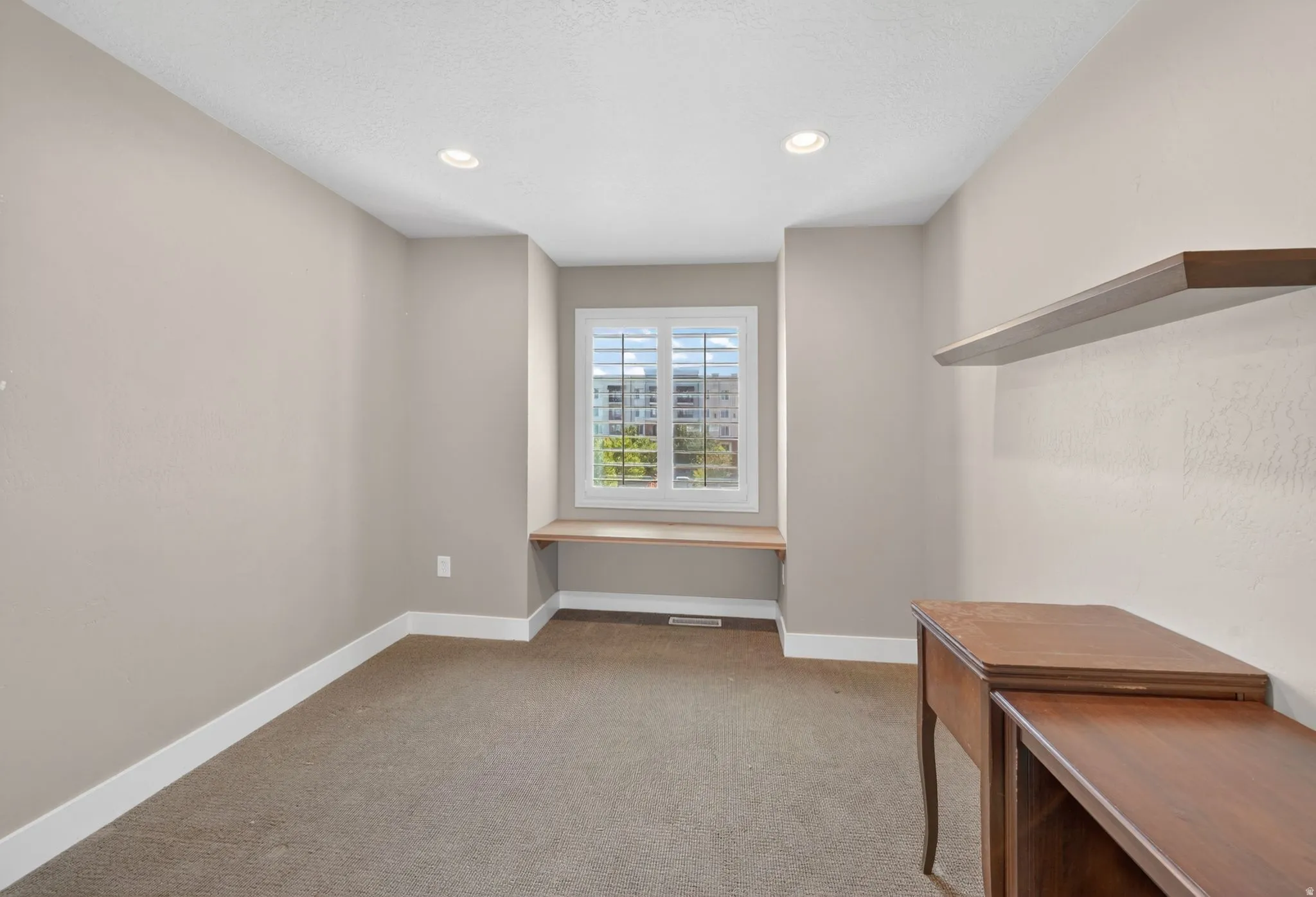 Built-in desk space featuring a window with plantation shutters, recessed lighting, and a floating wood-finish shelf