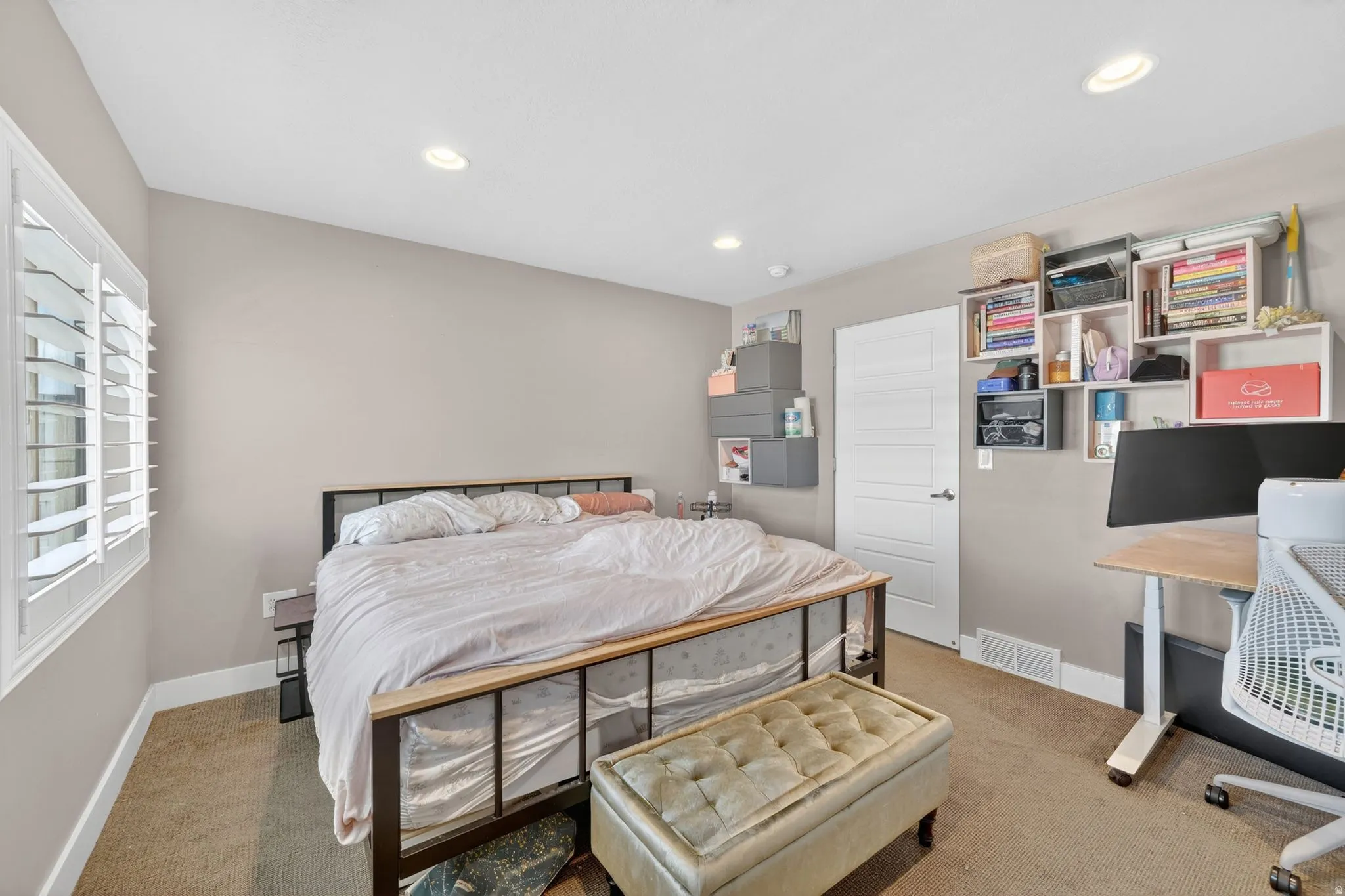 Carpeted bedroom featuring white plantation shutters, recessed lighting, and a modern paneled door