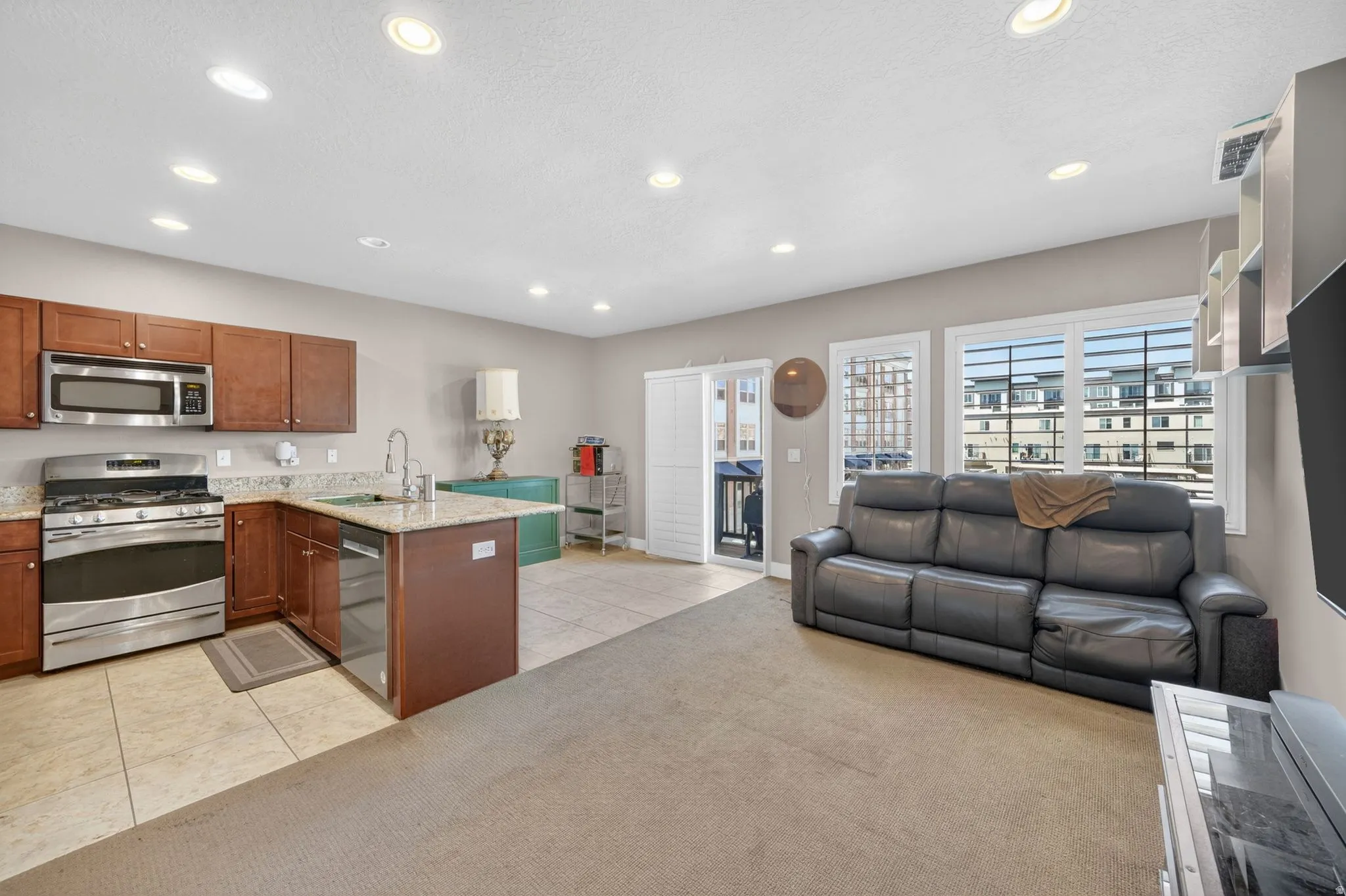 Open-concept living area featuring a kitchen with wood cabinetry, stainless steel appliances, and a granite-finish countertop island with a sink