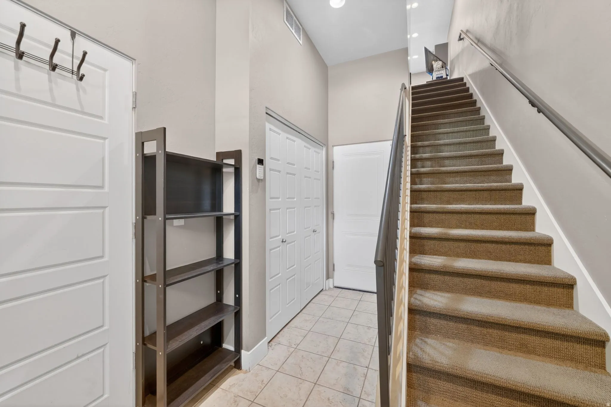 Entryway featuring tiled flooring, a paneled door with built-in coat hooks, and a carpeted staircase with a metal handrail