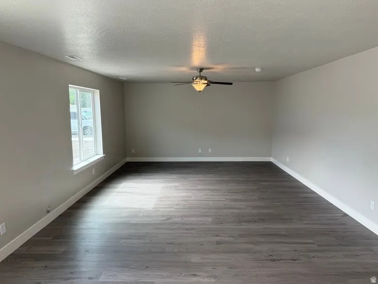 Spacious interior room featuring wood-finish flooring, neutral wall paint, white trim, a ceiling fan, and a window with white framing