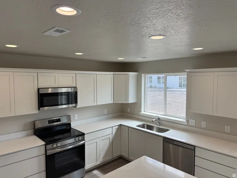Kitchen featuring white shaker cabinetry, stainless steel appliances, light-toned countertops, a stainless steel sink, and recessed lighting