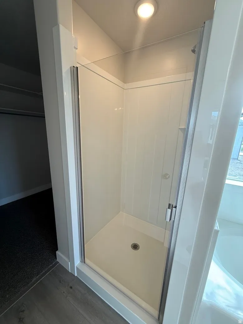 Walk-in shower featuring a clear glass enclosure, white paneling, and a light-colored shower base