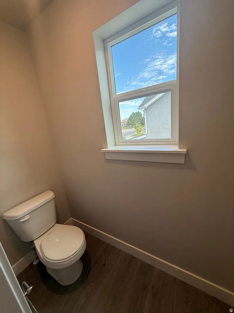 Compact water closet featuring a single-pane window, wood-finish flooring, white baseboards, and neutral wall tones