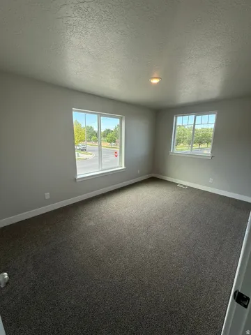 Spacious room featuring neutral paint, two large windows, durable carpeting, recessed ceiling lighting, and white baseboards