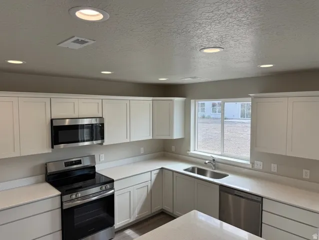 Kitchen featuring white shaker cabinetry, stainless steel appliances, light-toned countertops, a stainless steel sink, and recessed lighting