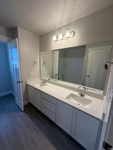 Dual vanity with white cabinetry, integrated sinks, light-toned countertops, and a full-width mirror