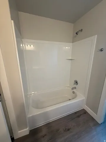Bathtub and shower combination unit featuring white acrylic surround, chrome fixtures, and a corner shelf