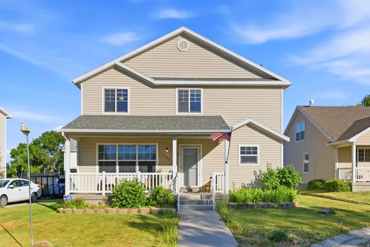 Two-story residence featuring light-toned horizontal siding, a covered front porch with white railings, and a concrete walkway