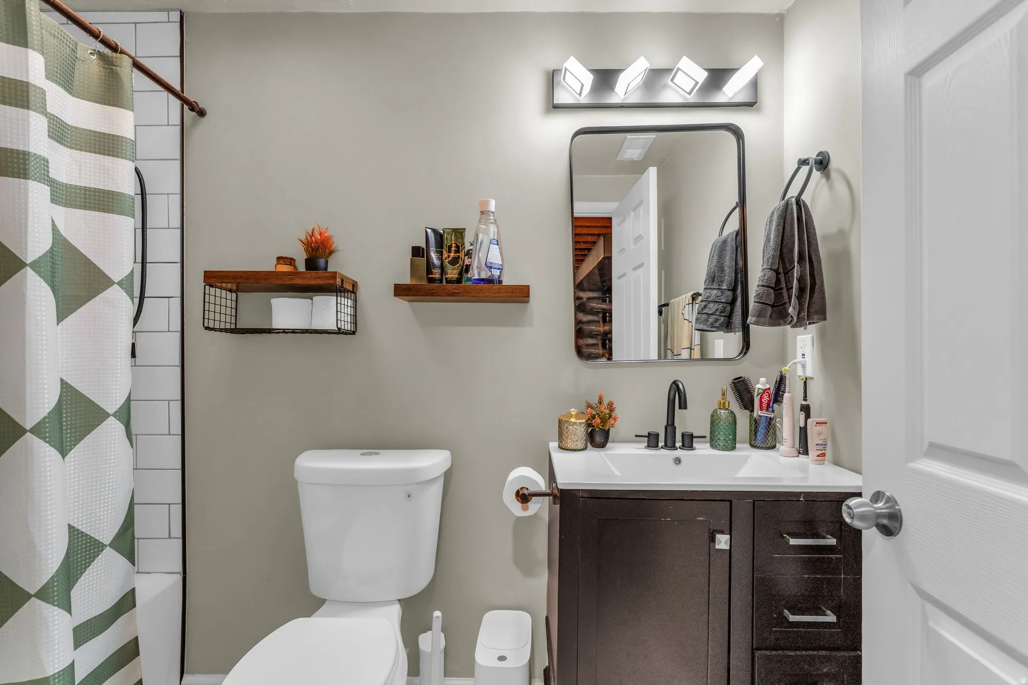 Bathroom featuring a dark wood vanity with white countertop, black fixtures, rectangular framed mirror, and modern vanity lighting