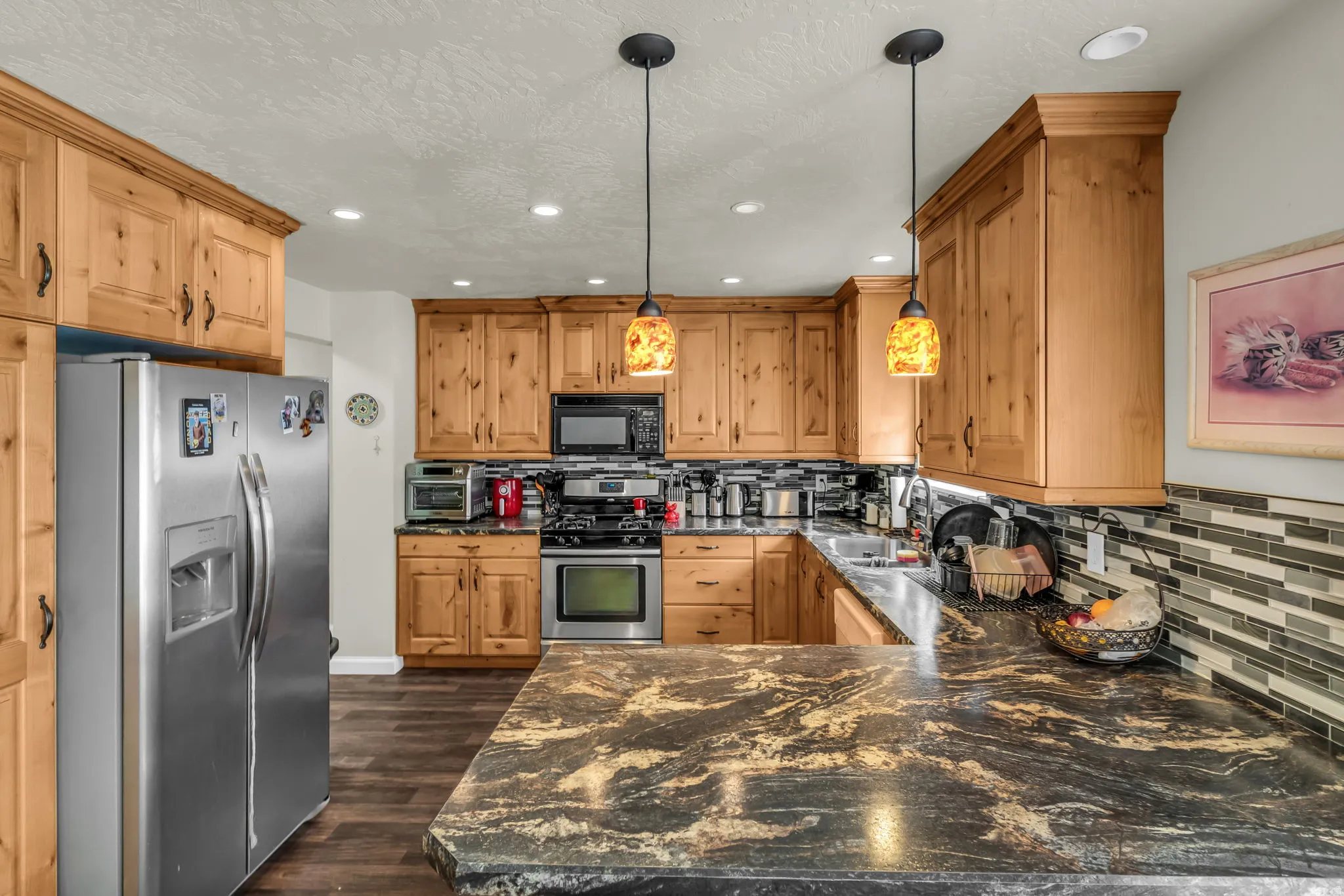 Kitchen featuring an expansive island with a dark granite countertop, natural wood cabinetry, stainless steel appliances, and recessed lighting