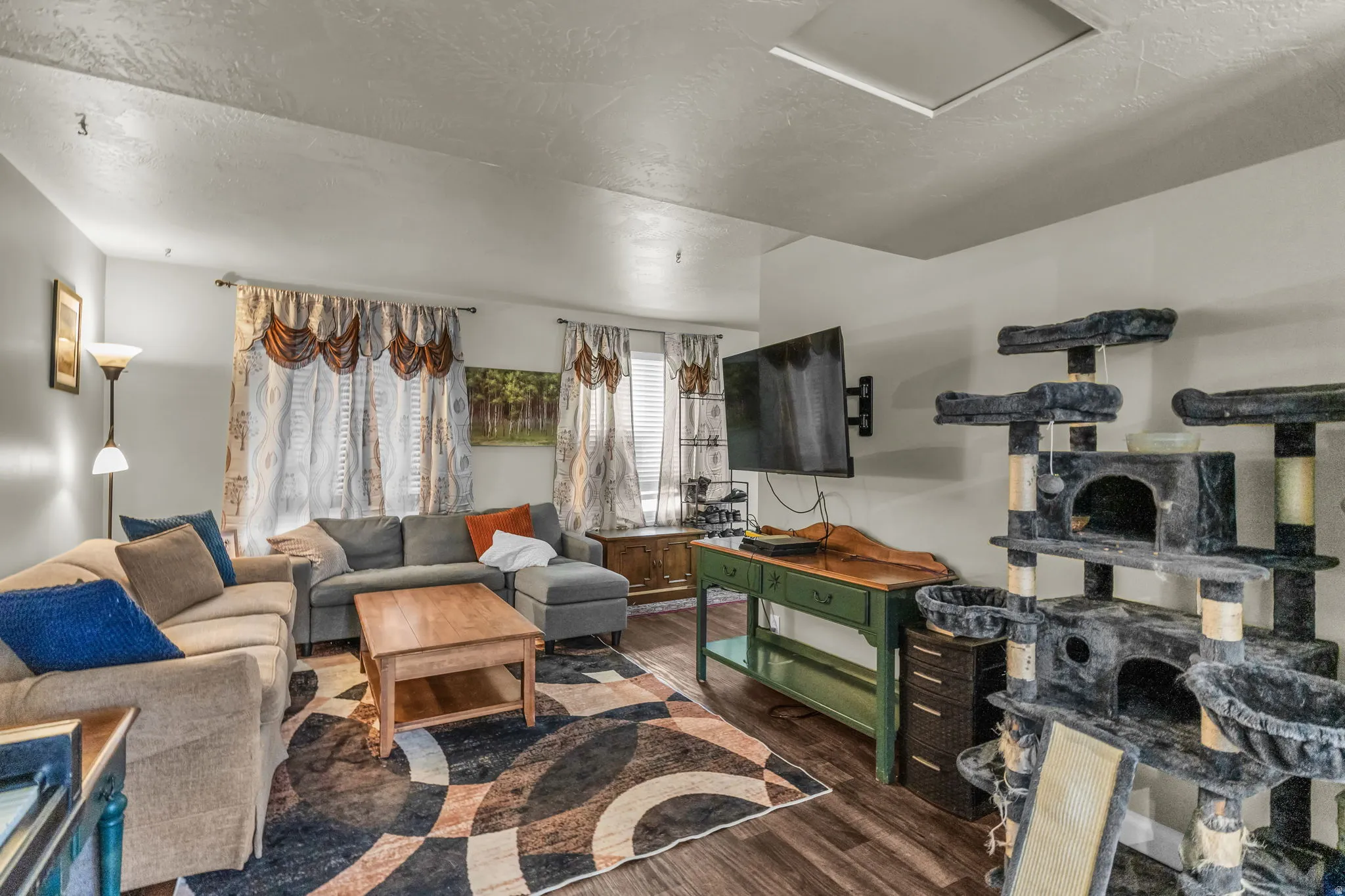 Spacious living area featuring wood-finish flooring, light-toned walls, and multiple windows with blinds