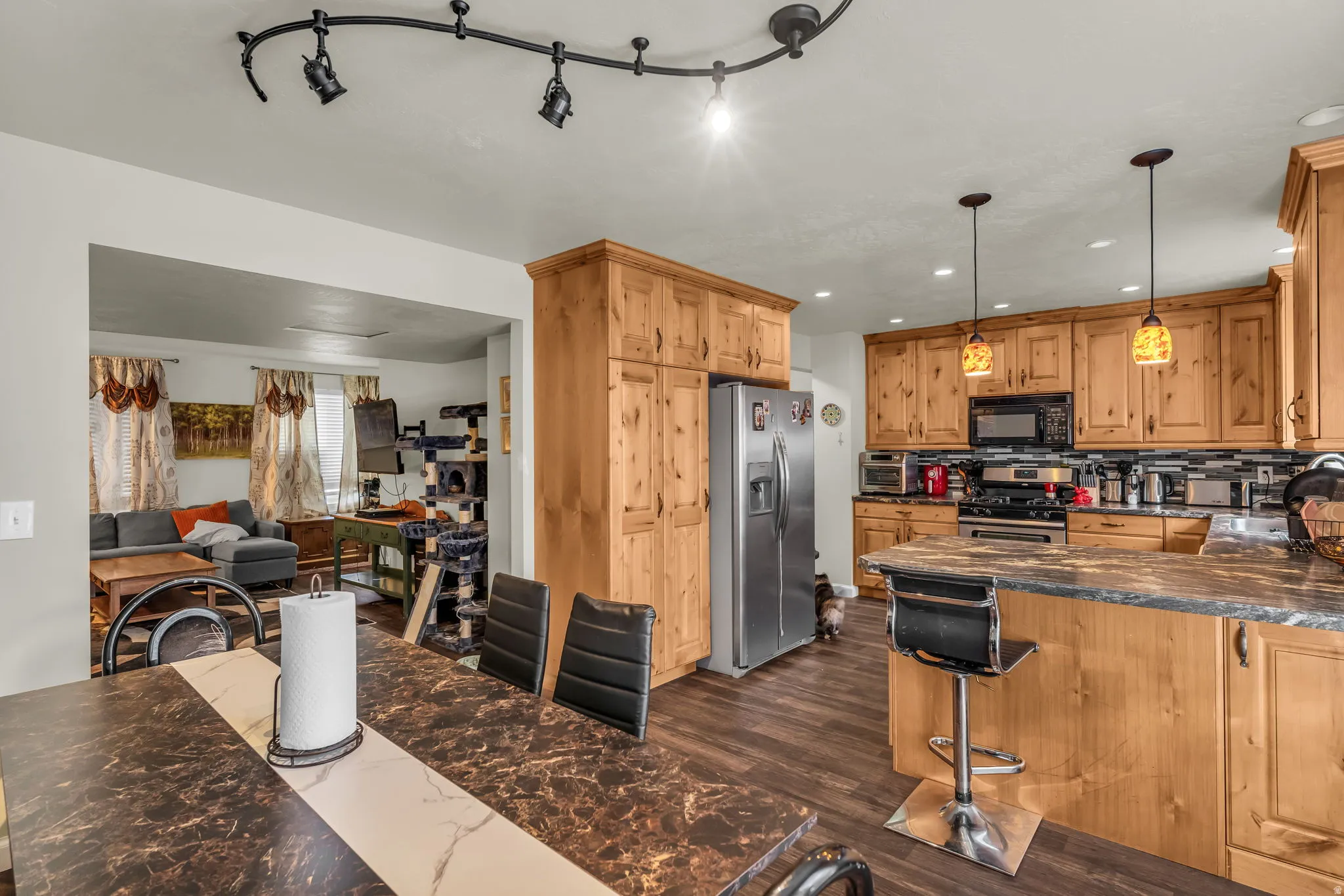 Kitchen featuring natural wood-finish cabinetry, stainless steel appliances, dark stone-finish countertops, and a tile backsplash