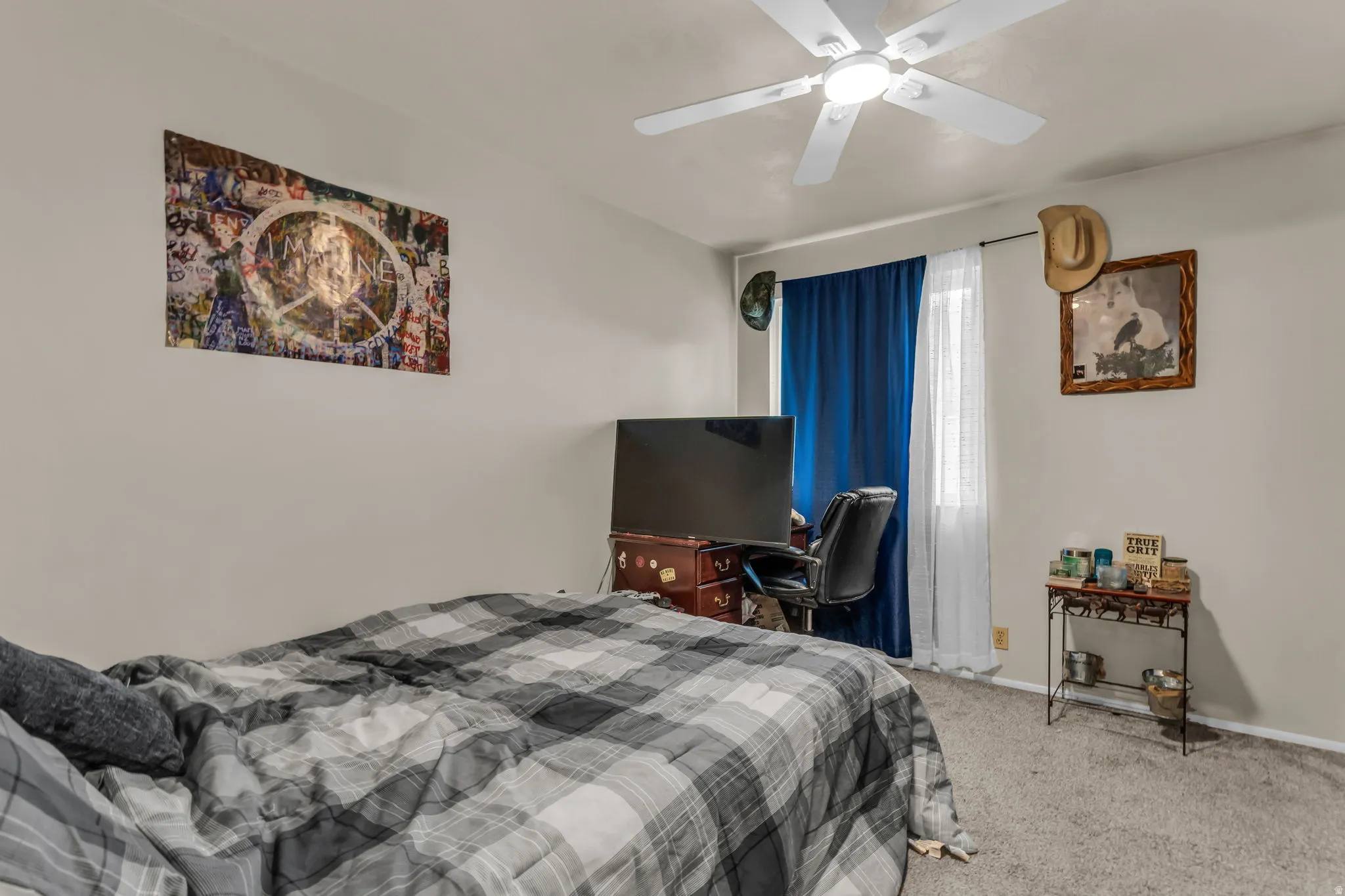 Bedroom featuring neutral wall paint, gray carpet flooring, a ceiling fan with light fixture, and a window with blinds and blue drapes