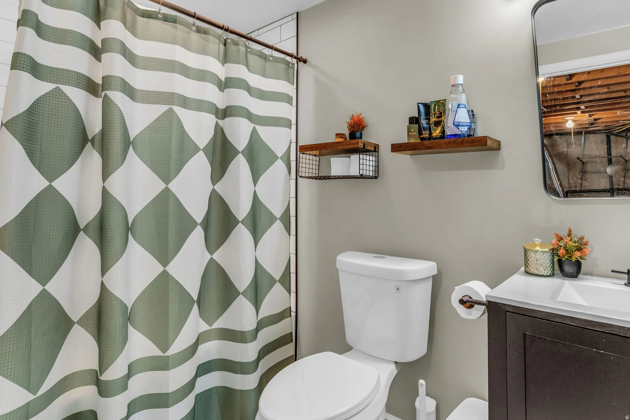 Bathroom featuring a white toilet, dark wood-finish vanity with an integrated sink, black-framed mirror, and wall-mounted shelving