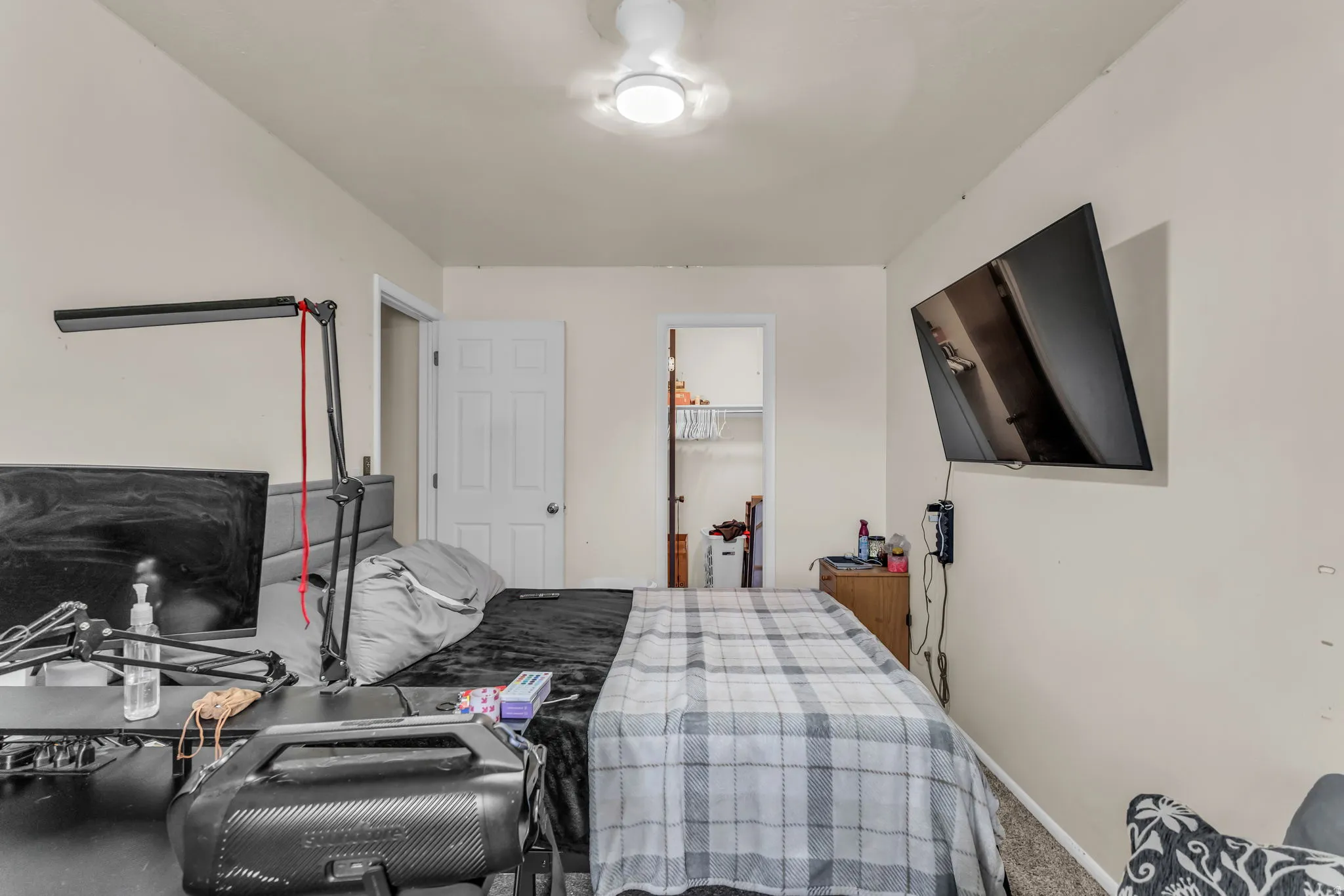 Bedroom featuring neutral wall tones, textured carpet flooring, a ceiling fan with integrated lighting, and a closet with shelving