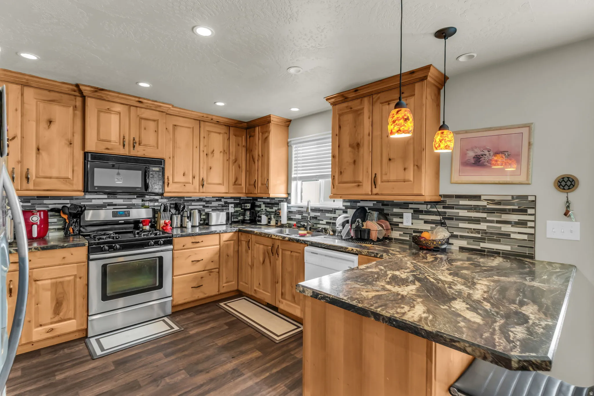 Kitchen featuring wood cabinetry, stainless steel appliances, dark wood-finish flooring, and a multi-toned tile backsplash