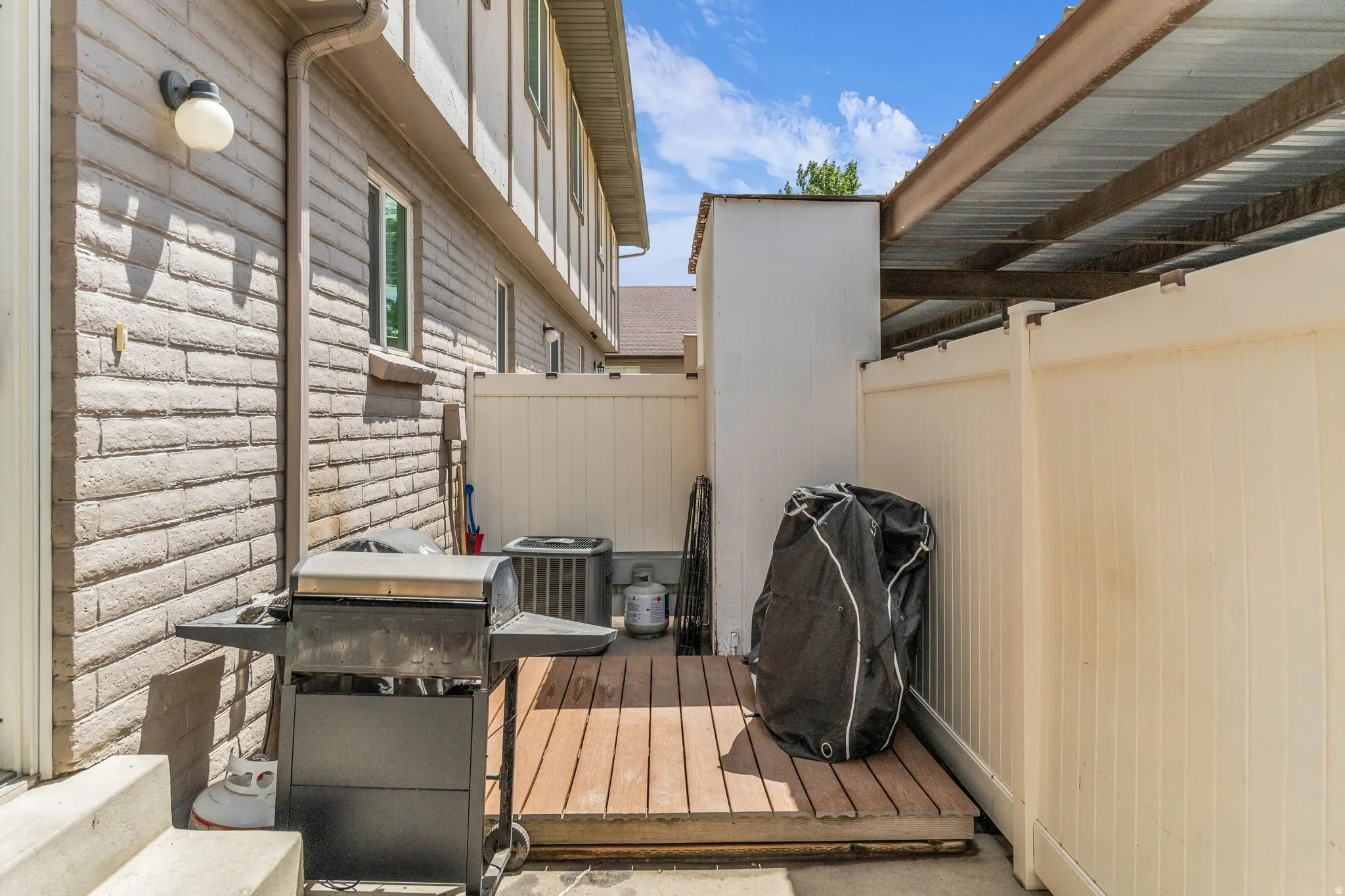 Exterior space featuring a brick facade, privacy fencing, wood-finish decking, and a covered patio area