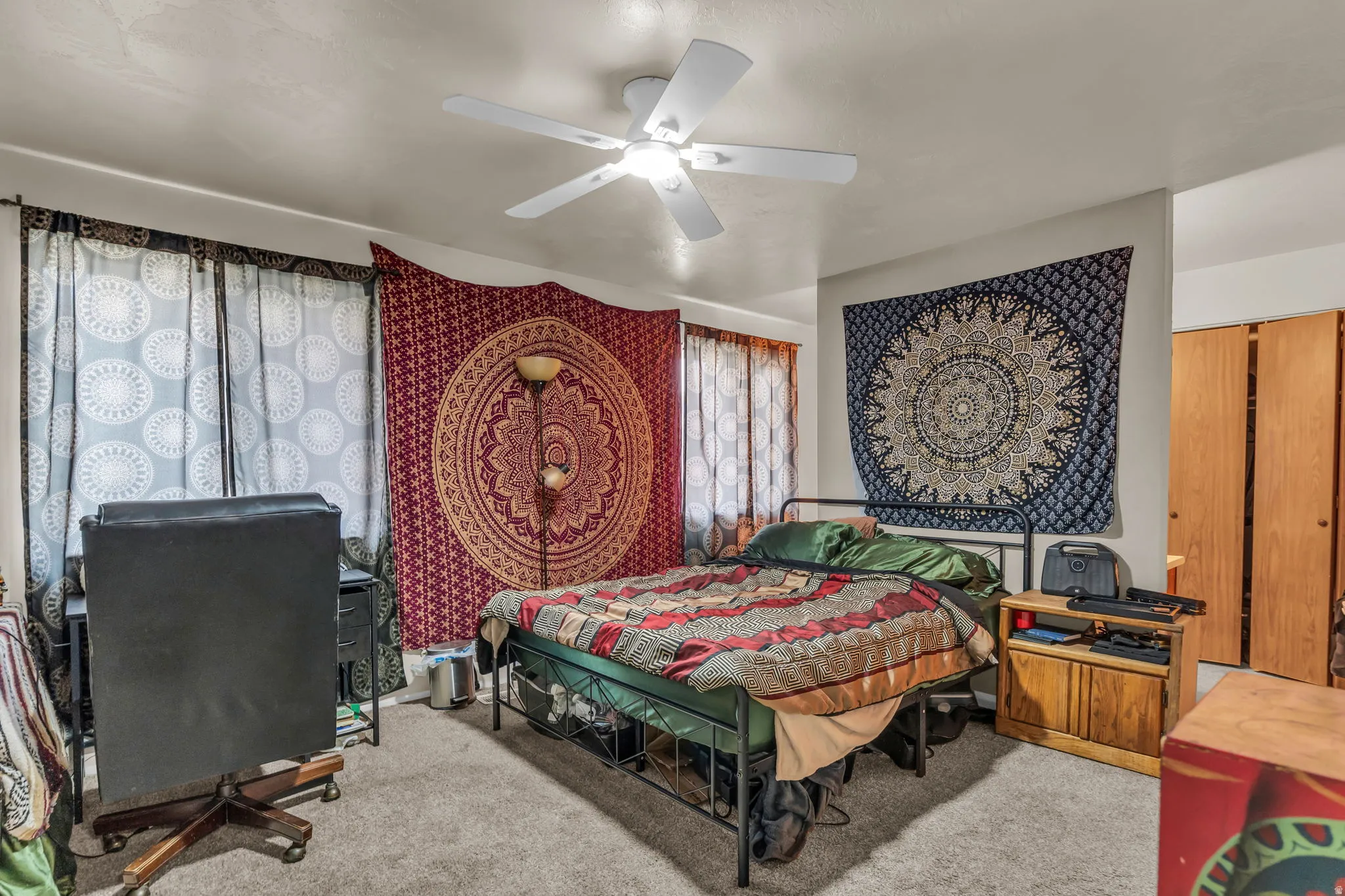Carpeted room with a ceiling fan light fixture, two windows with curtains, and bifold closet doors