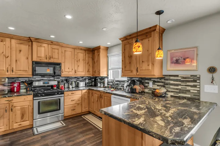 Kitchen featuring wood-finish cabinetry, stainless steel appliances, dark countertops, and a mosaic tile backsplash