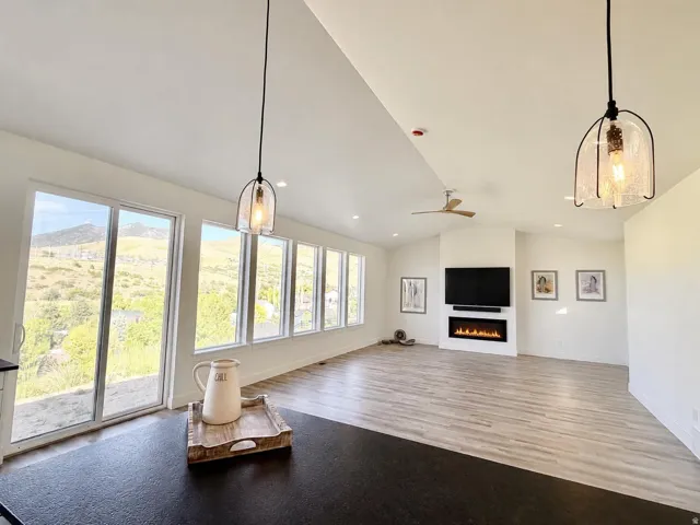 Expansive room featuring vaulted ceilings, a linear electric fireplace, wood-finish flooring, a wall of windows, and a sliding glass door